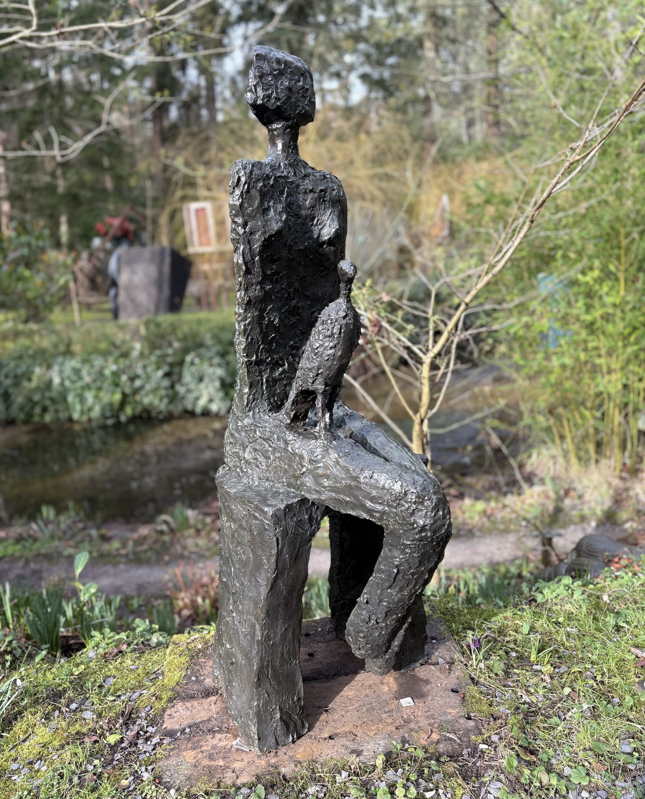 Companion by Wendy Fisher is a simple figurative bronze sculpture of a seated woman with a kestrel bird on her lap.