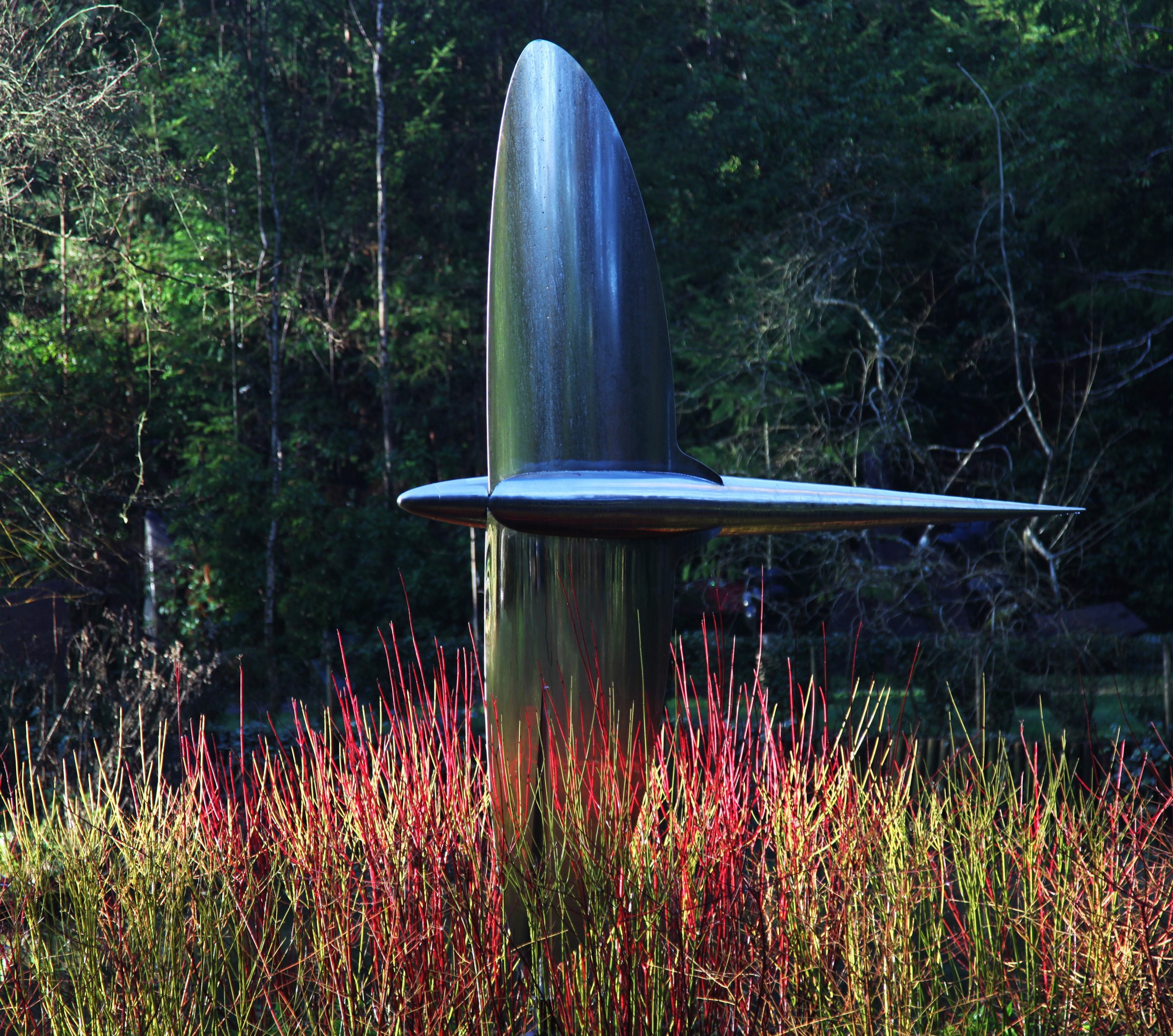 A kinetic mirror polished stainless steel sculpture of a aeroplane flying on its side.