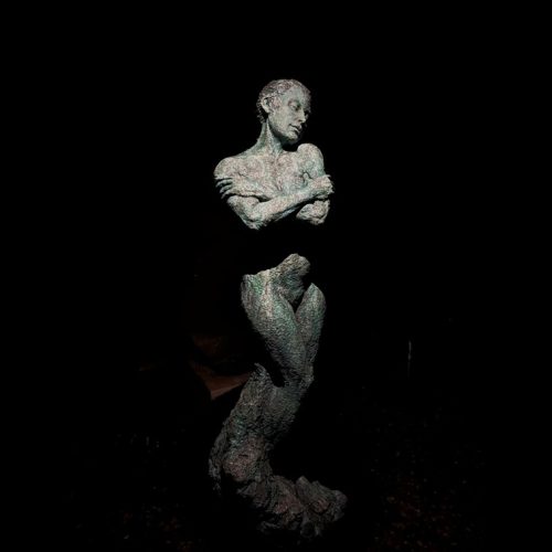 Emergence by Brendon Murless. Bronze figurative sculpture of a woman with her arms crossed in a self embrace and a contented expression. Blue green patina.