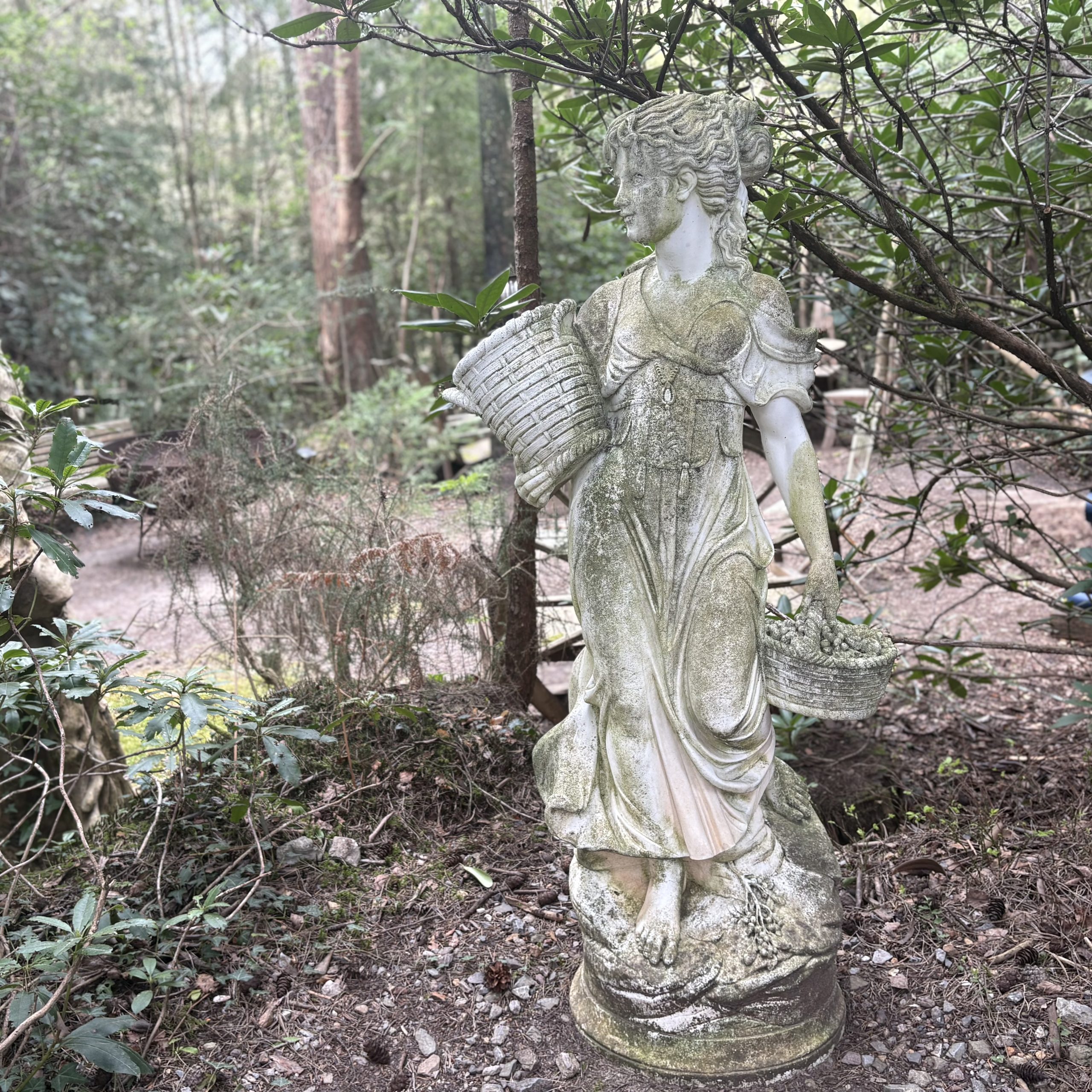 Lady Carrying Baskets by After The Antique is a cast stone, weather-aged sculpture of a girl going to market suitable for outdoor display