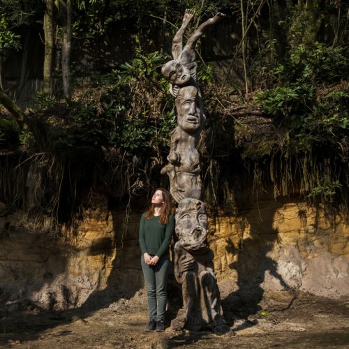 Antique Totem Pole is a Monumental carved hardwood totem pole–style outdoor tribal sculpture featuring stacked grotesque figures