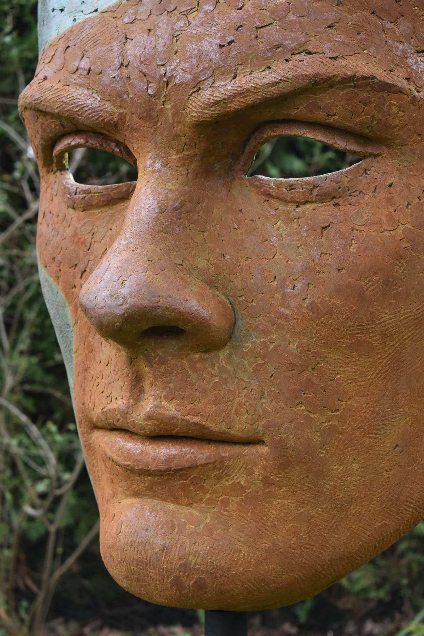 Mask of Achilles by Nicola Godden. A large bronze resin mask sculpture of the face of the Greek warrior, Achilles. Displayed on top of a wooden plinth.
