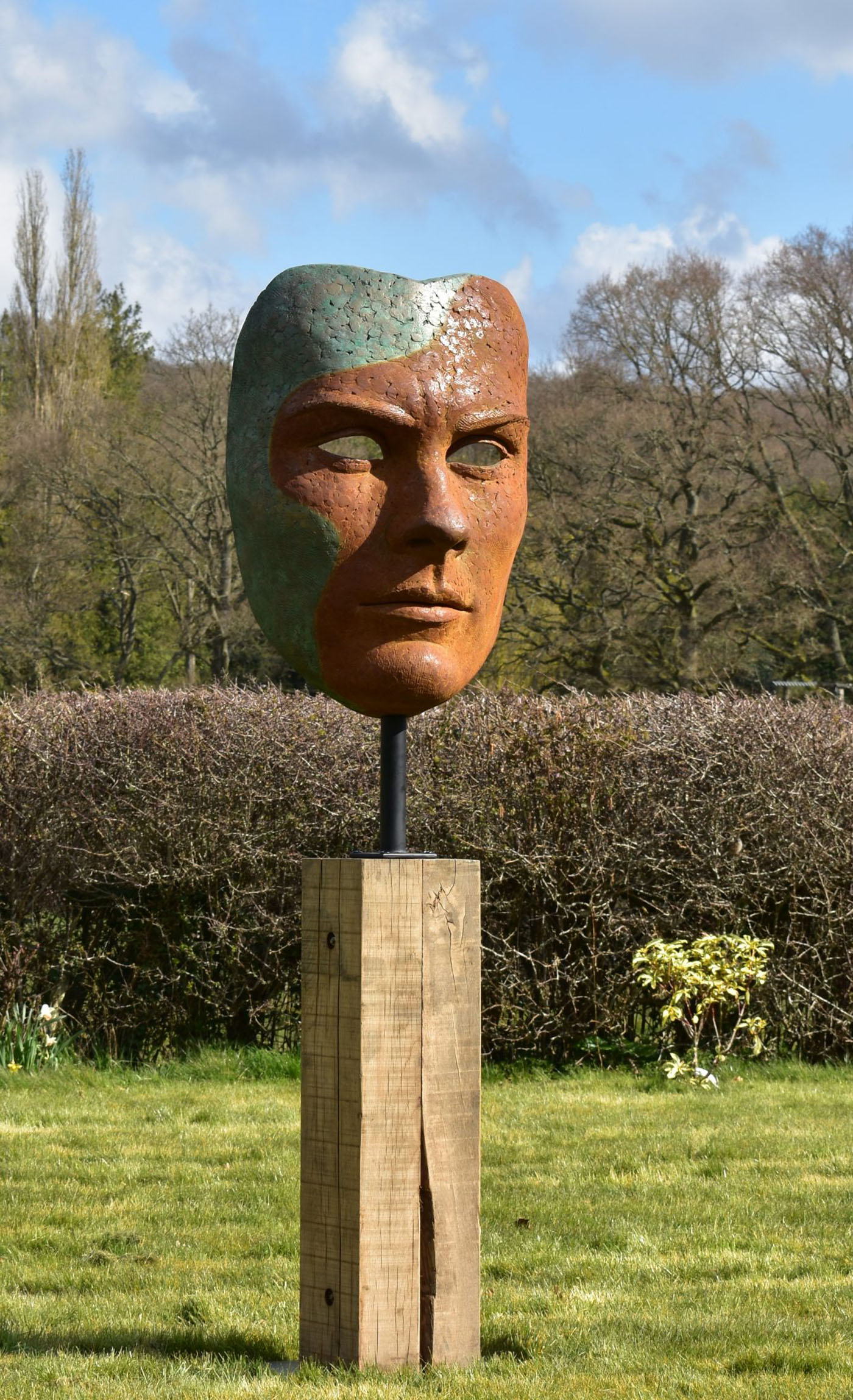 Mask of Achilles by Nicola Godden. A large bronze resin mask sculpture of the face of the Greek warrior, Achilles. Displayed on top of a wooden plinth.