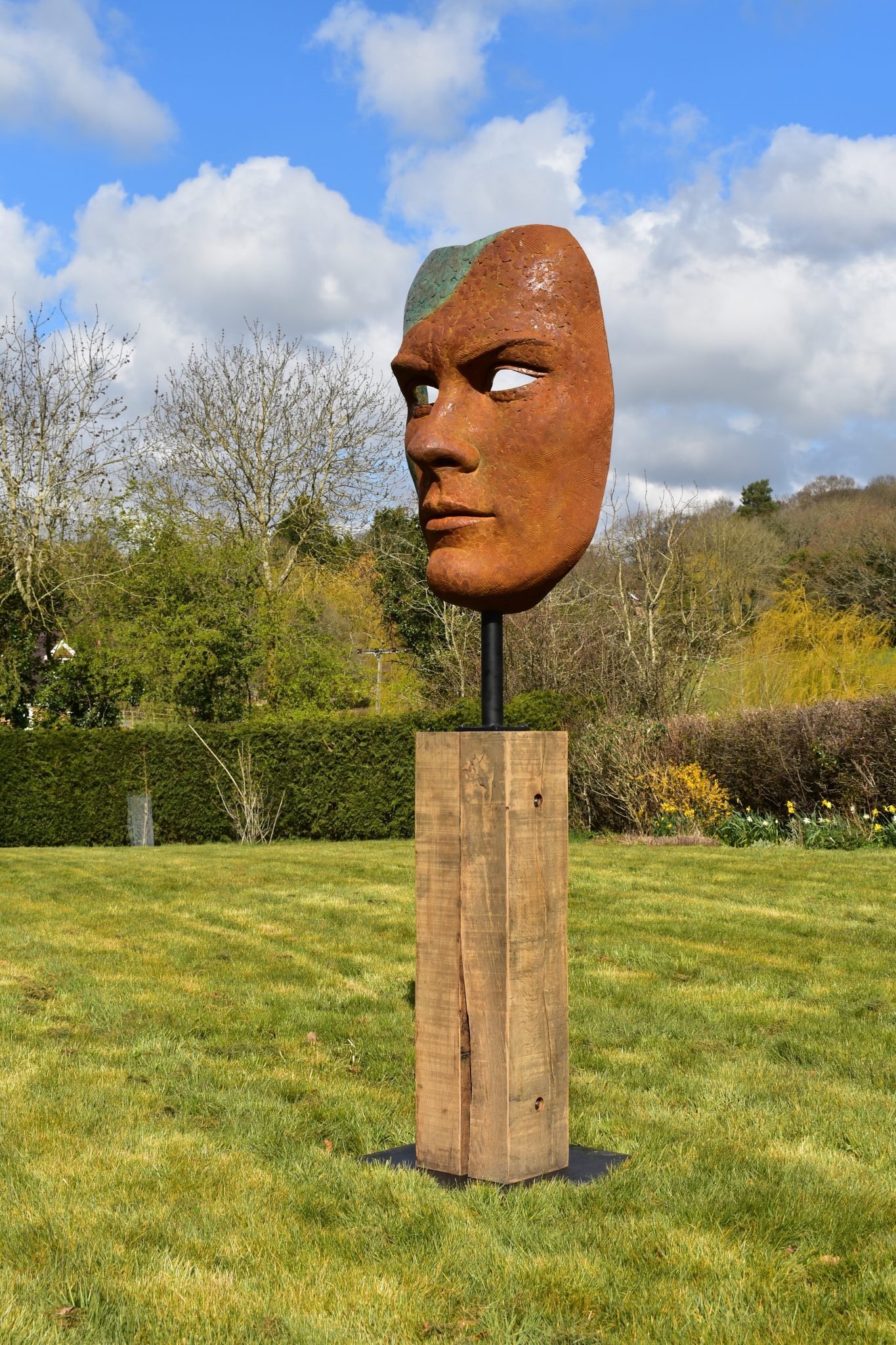 Mask of Achilles by Nicola Godden. A large bronze resin mask sculpture of the face of the Greek warrior, Achilles. Displayed on top of a wooden plinth.