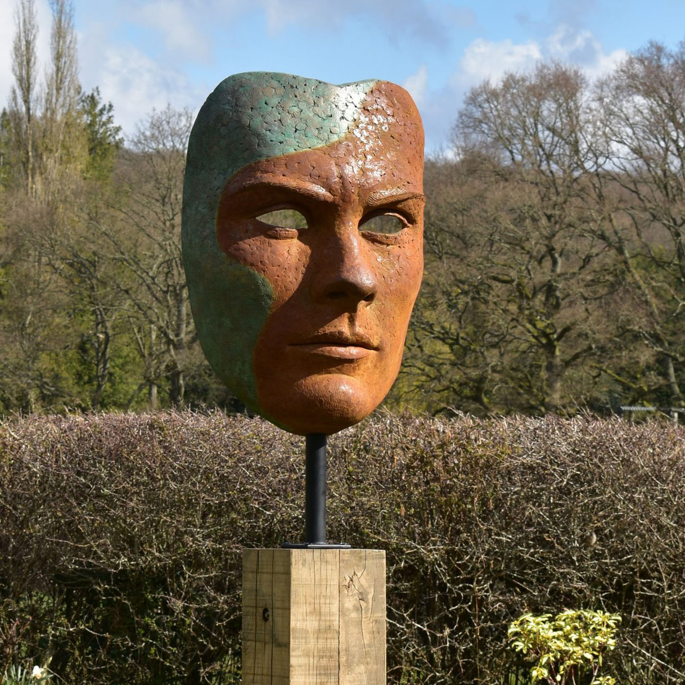 Mask of Achilles by Nicola Godden. A large bronze resin mask sculpture of the face of the Greek warrior, Achilles. Displayed on top of a wooden plinth.
