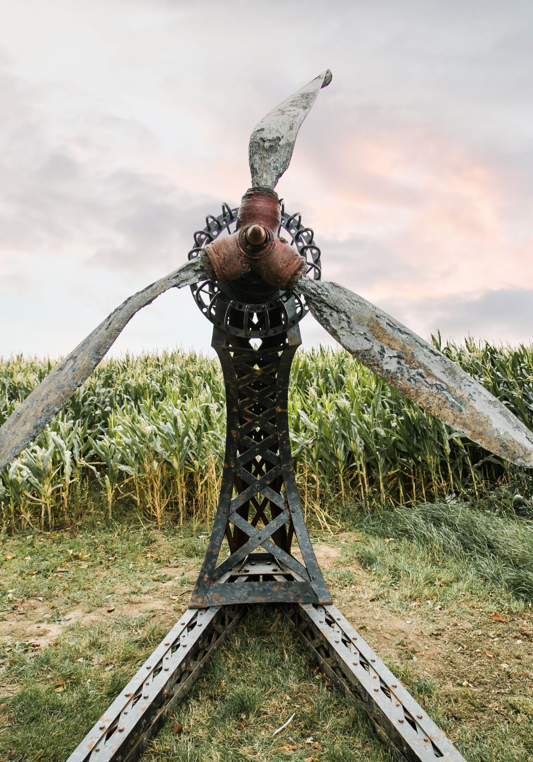 A architectural found object sculpture of a plane propeller mounted onto a metal frame.