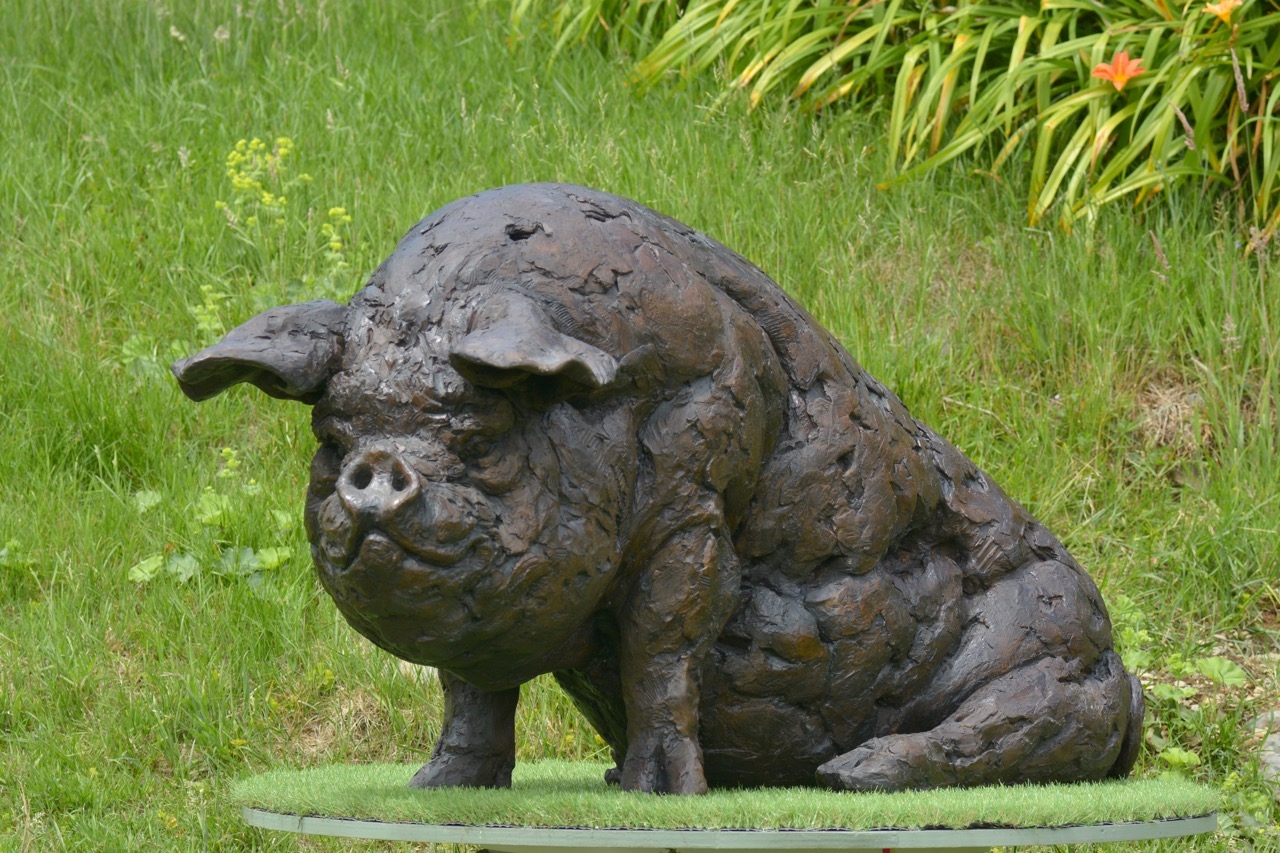 A realism bronze resin sculpture of a large pig sitting down.
