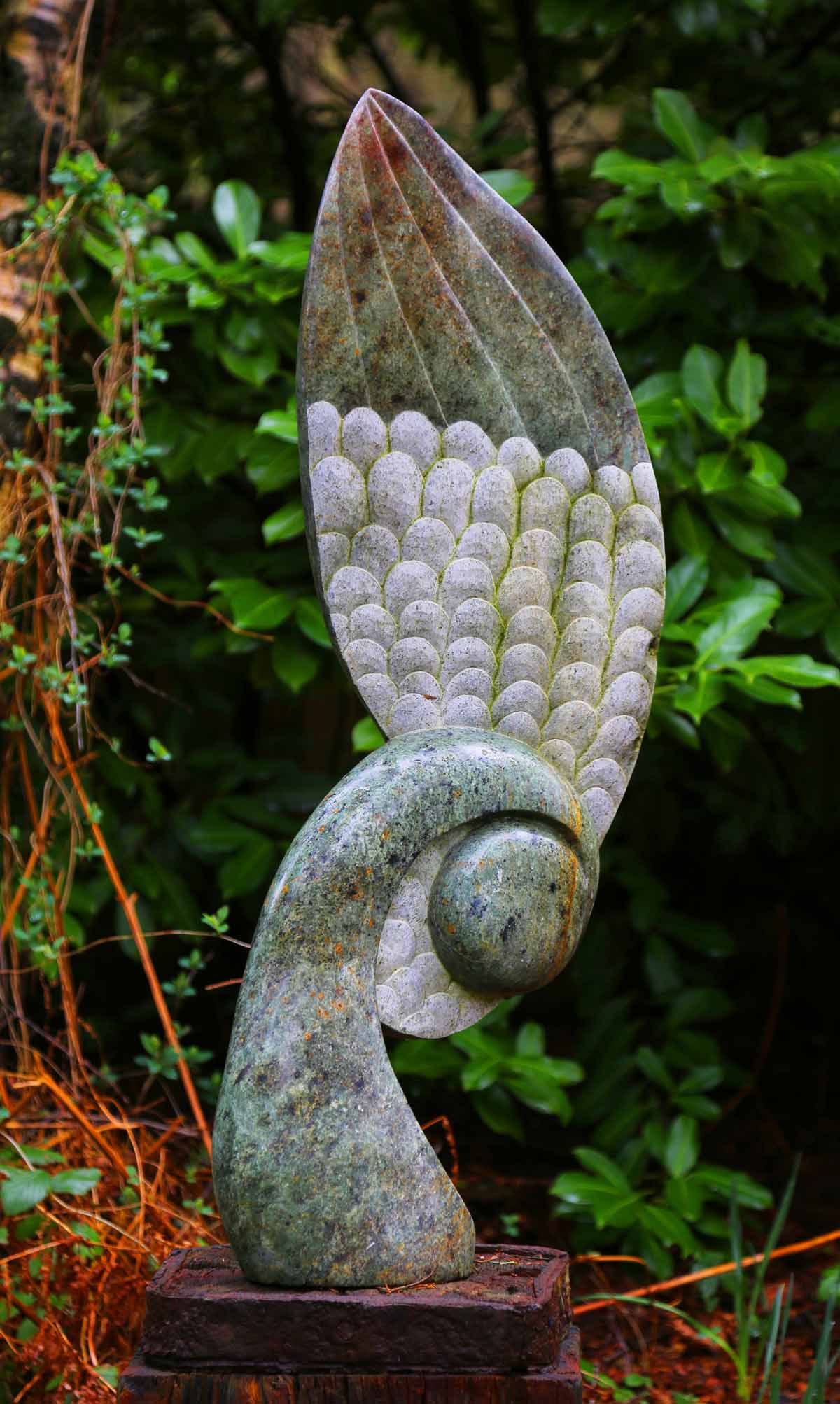 A shona opal stone sculpture of a seed pod with a large wing on the side of it.