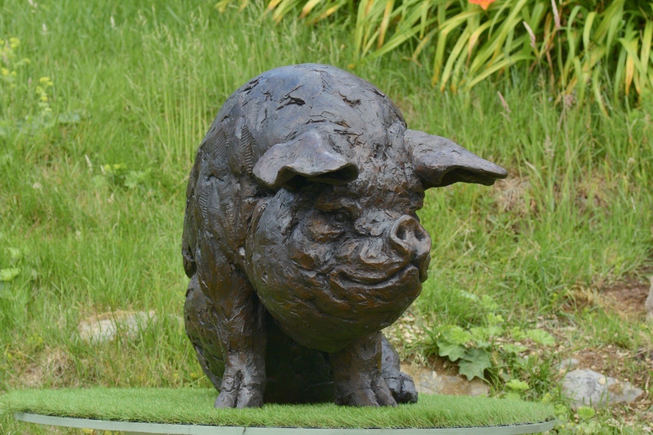 A realism bronze resin sculpture of a large pig sitting down.
