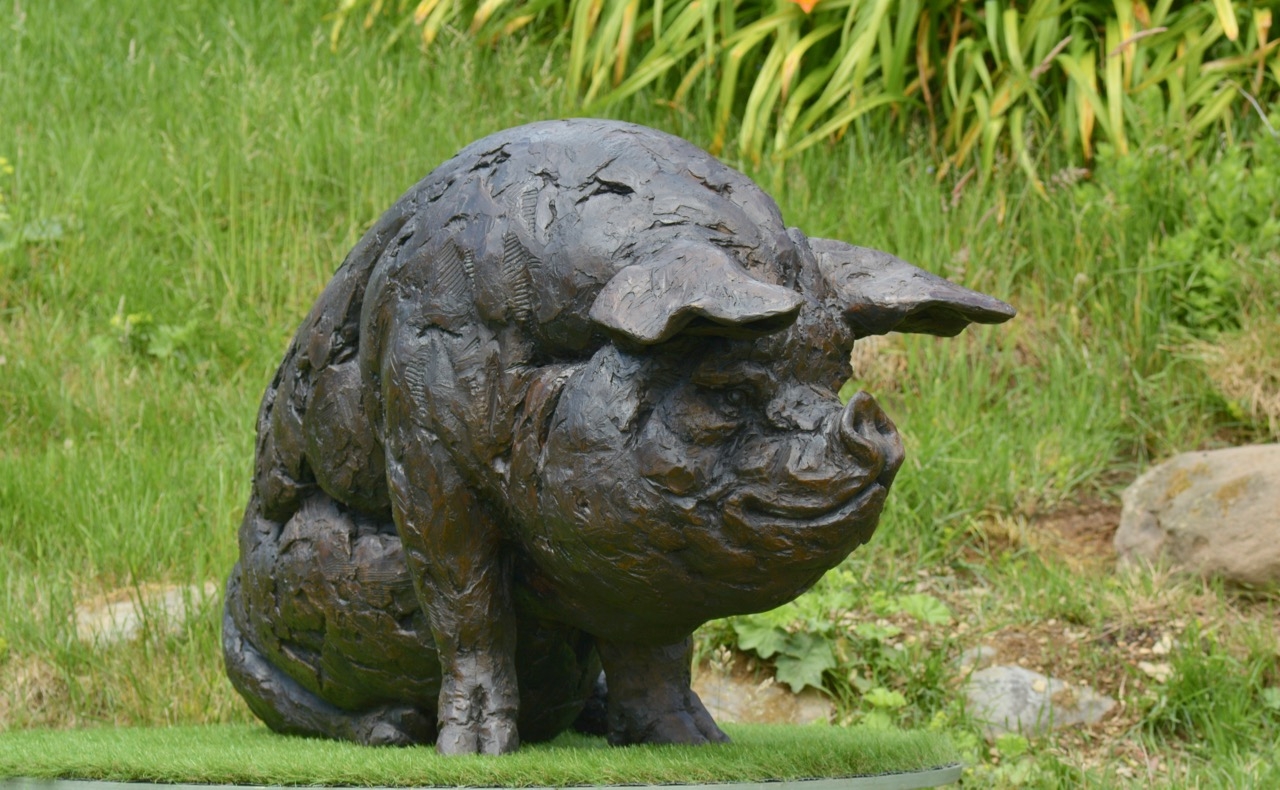 A realism bronze resin sculpture of a large pig sitting down.