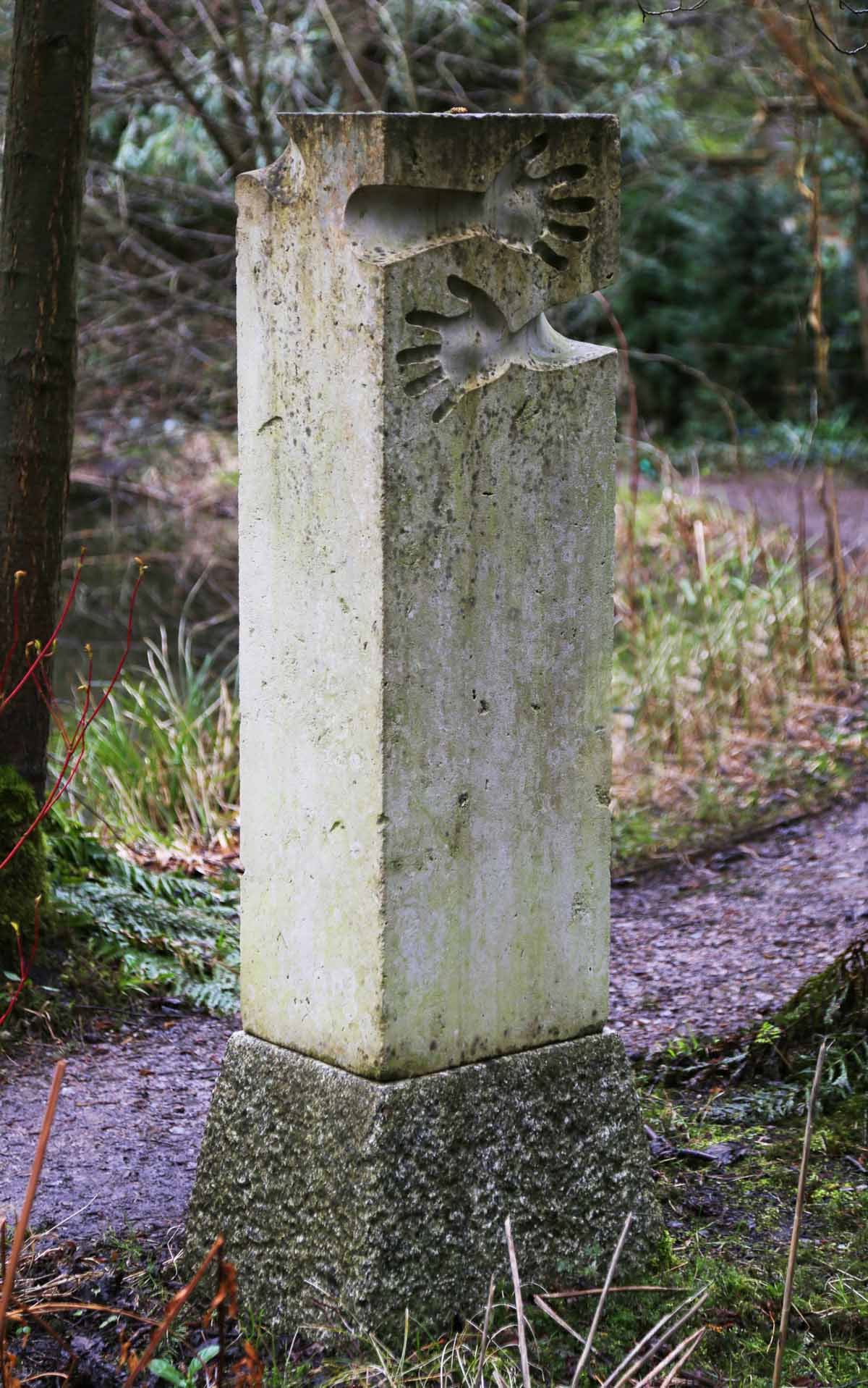 A minimalist portland stone sculpture of a block of stone with two arms carved onto one side.