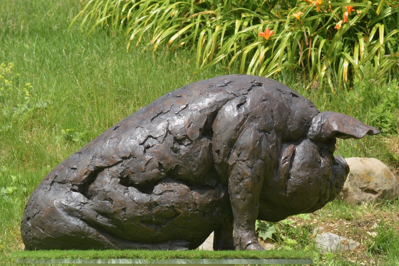 A realism bronze resin sculpture of a large pig sitting down.