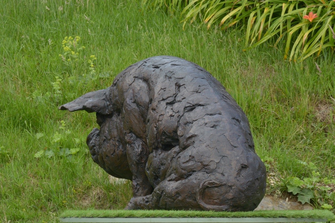 A realism bronze resin sculpture of a large pig sitting down.