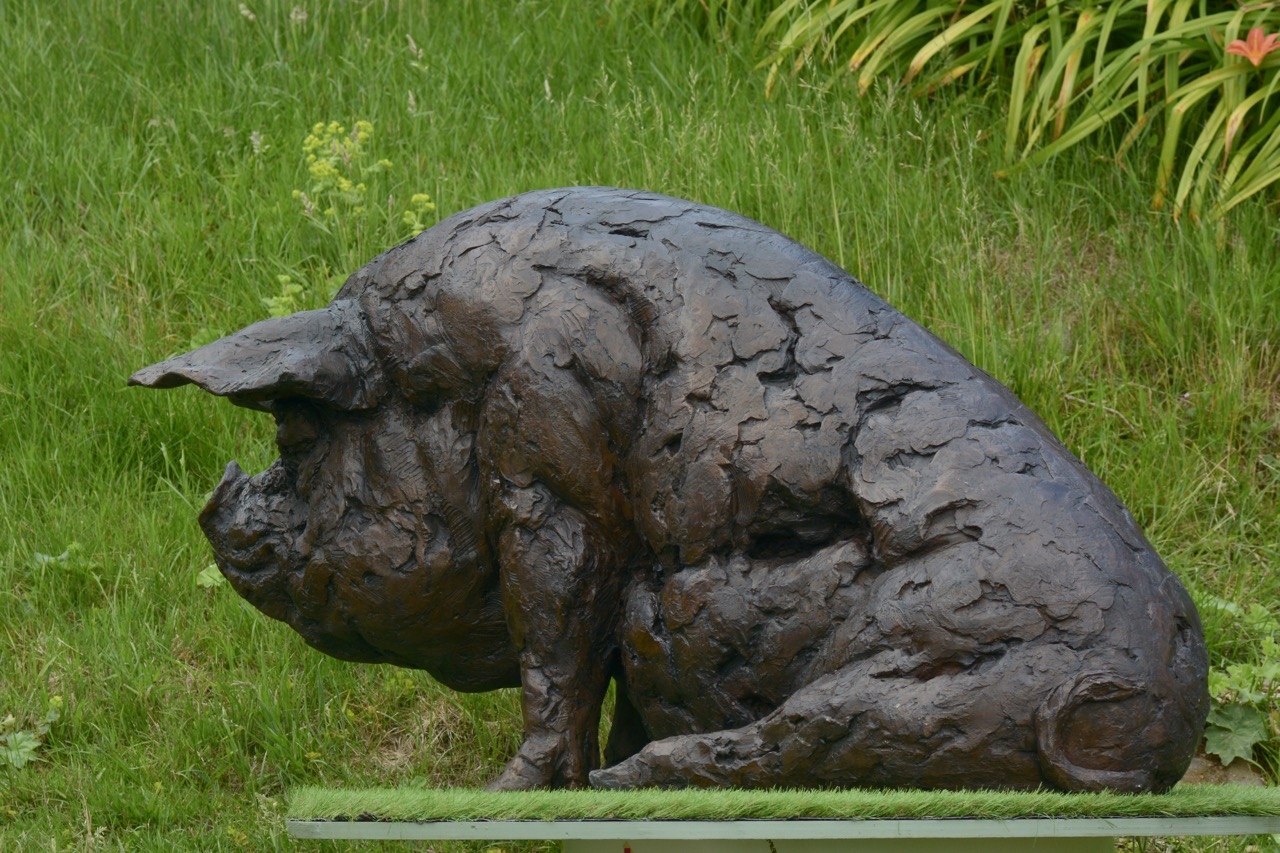 A realism bronze resin sculpture of a large pig sitting down.