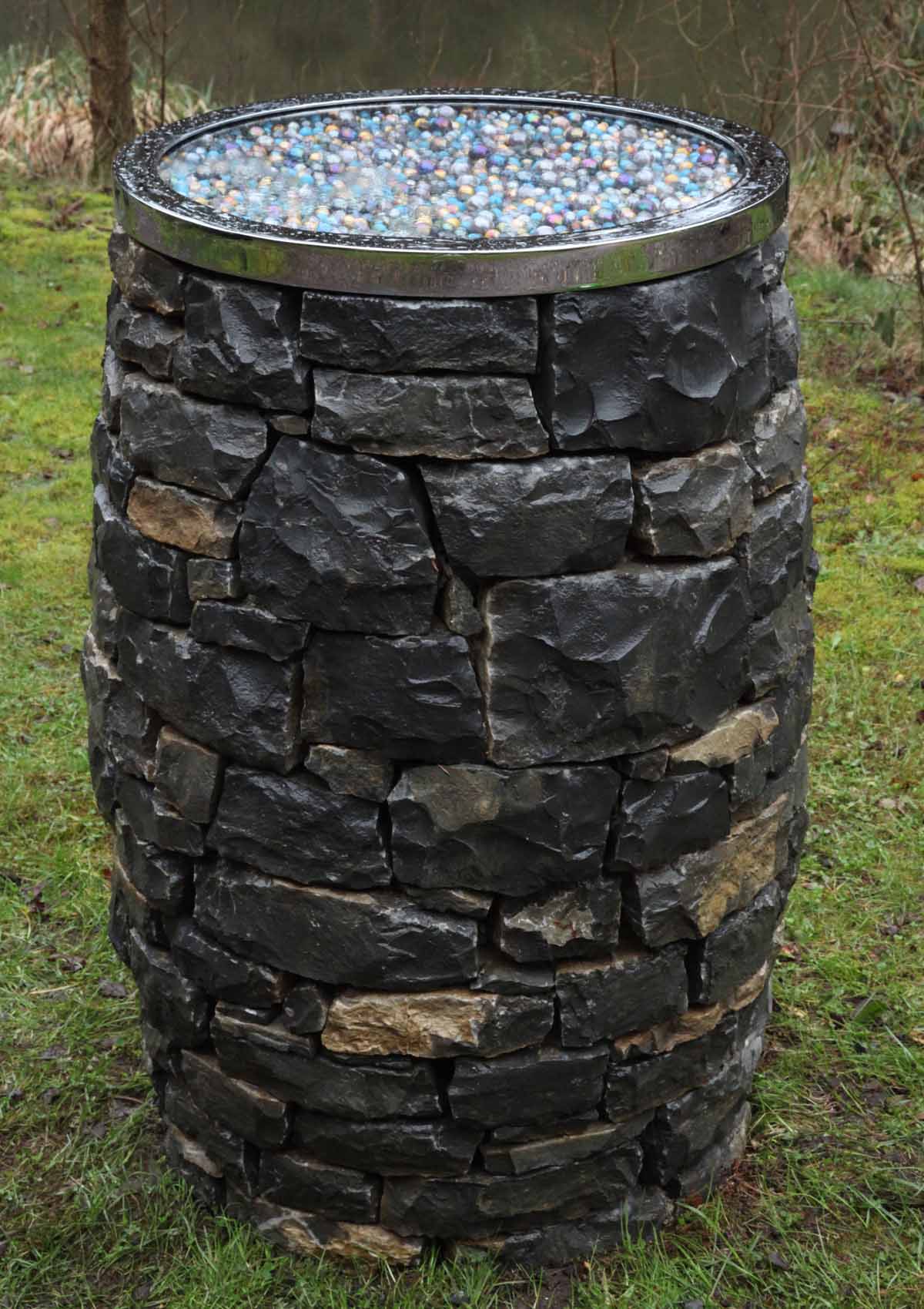 A furniture stone, steel and marble sculpture of a barrel shaped table with a marble covered top.