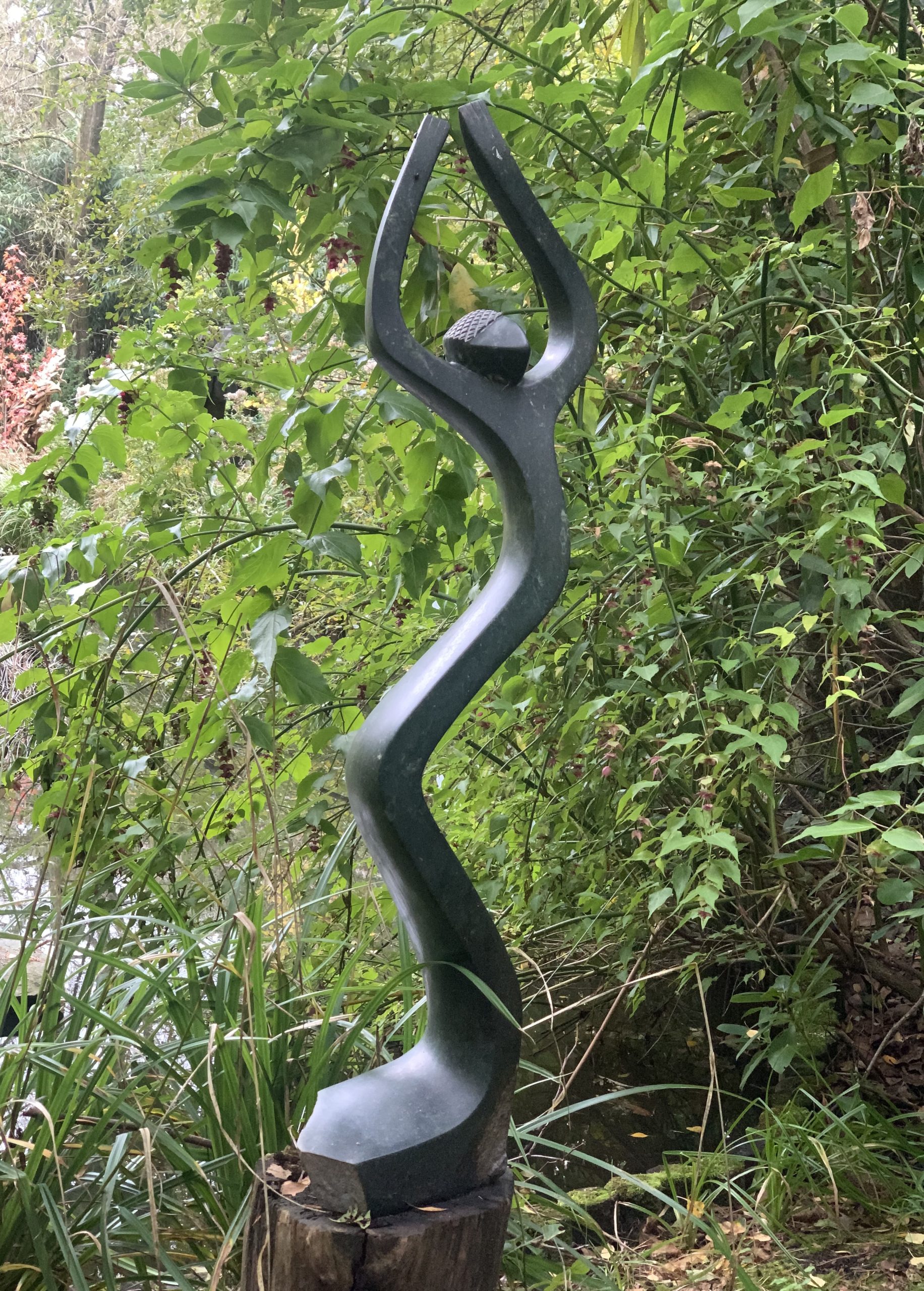 A shona opal stone sculpture of a figure stretching upwards.