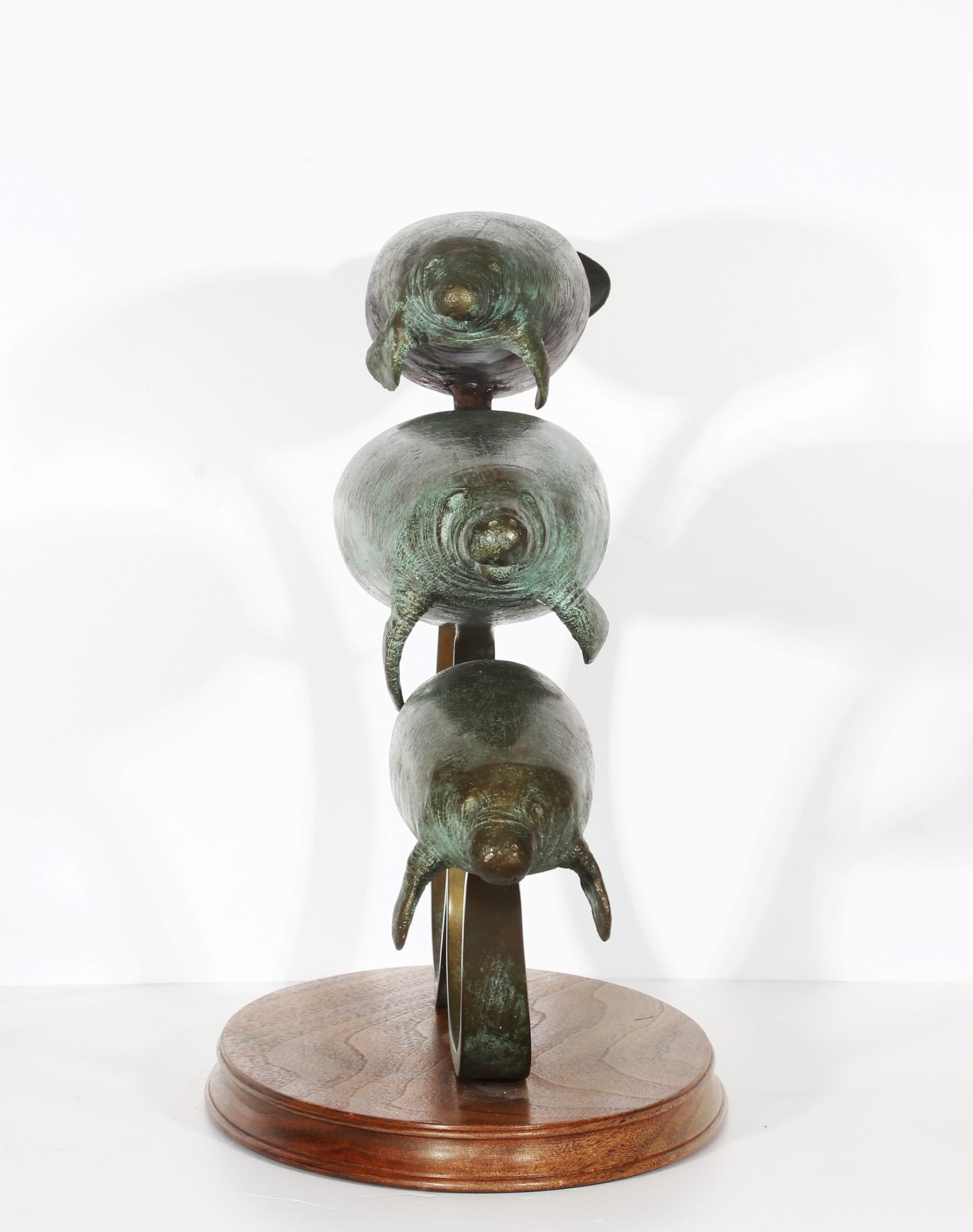 River Shadows by Andre Harvey is a Realistic bronze sculpture of 3 Manatees behind one another, each one slightly higher than the one before it. They are all being held up by a bronze rod to give them the effect of floating/swimming. On a wooden base.