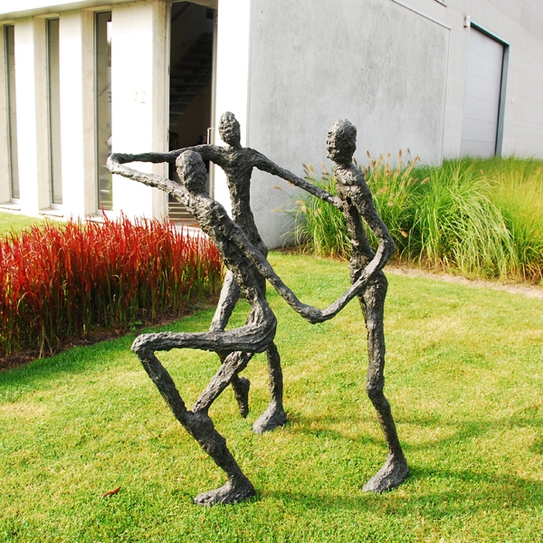 A figurative bronze sculpture of a group of three figures running and holding hands.