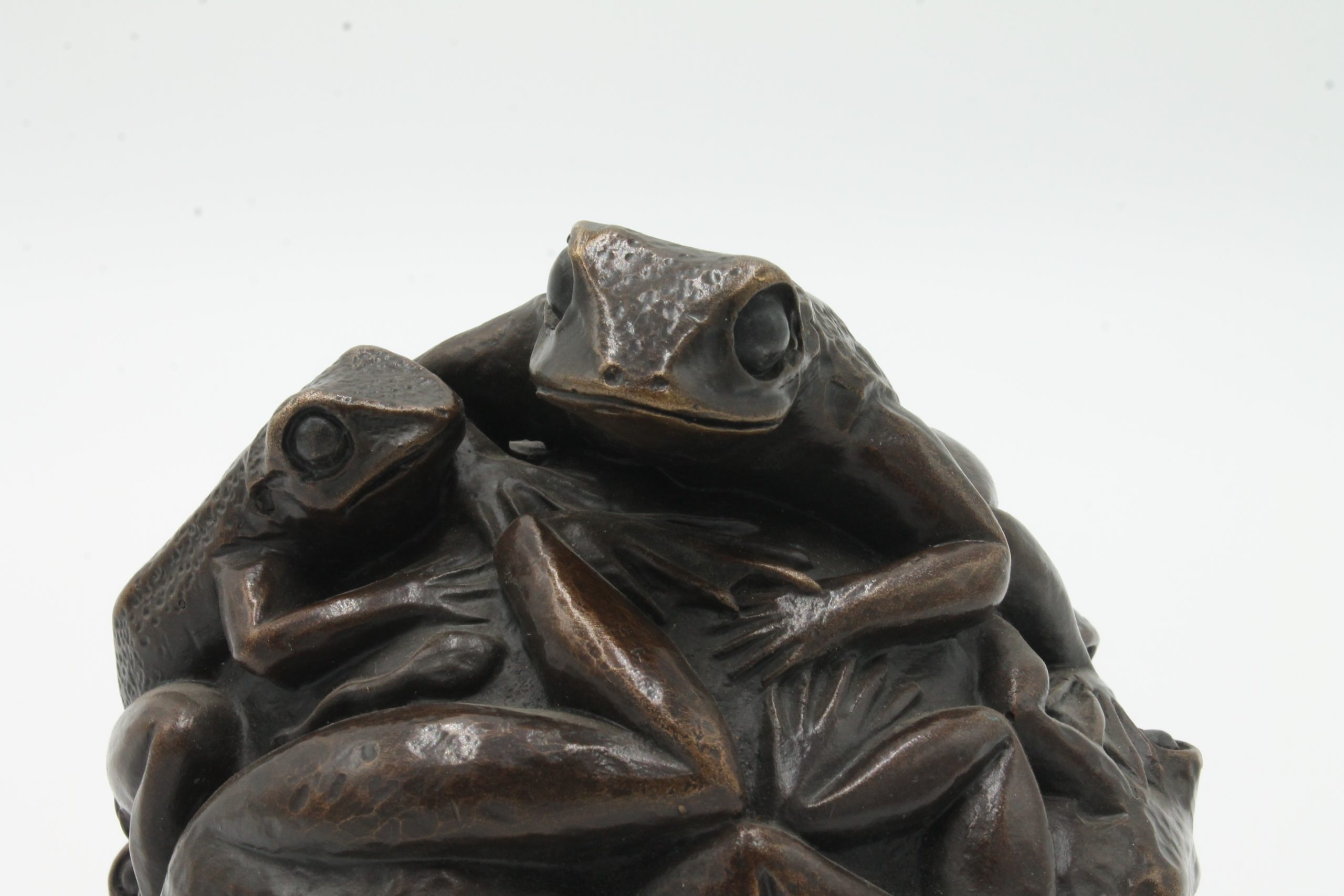 A contemporary bronze sculpture of a group of frogs all formed together into a ball.