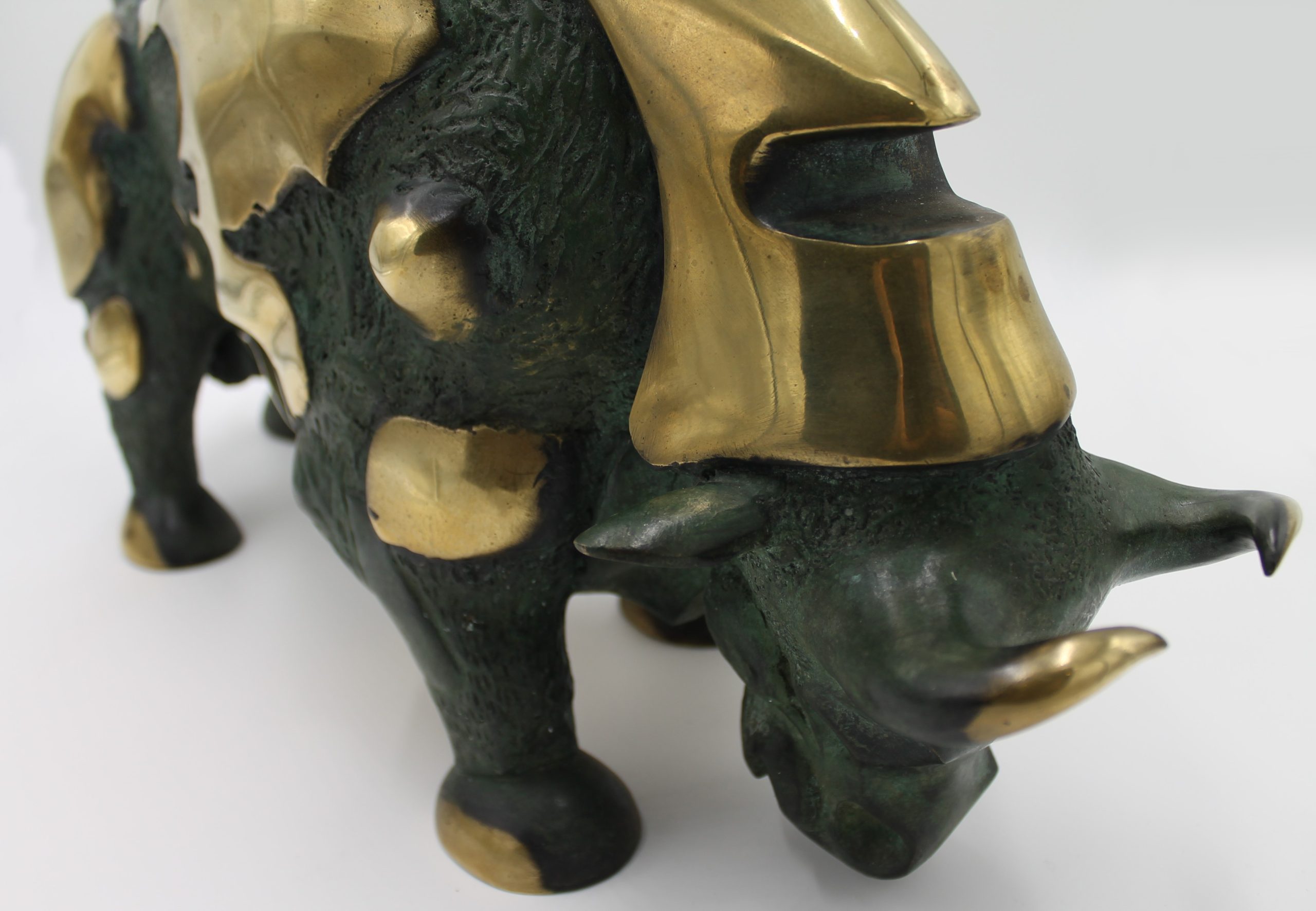 A abstract bronze sculpture of a bull with various patches of gold colouring over it.