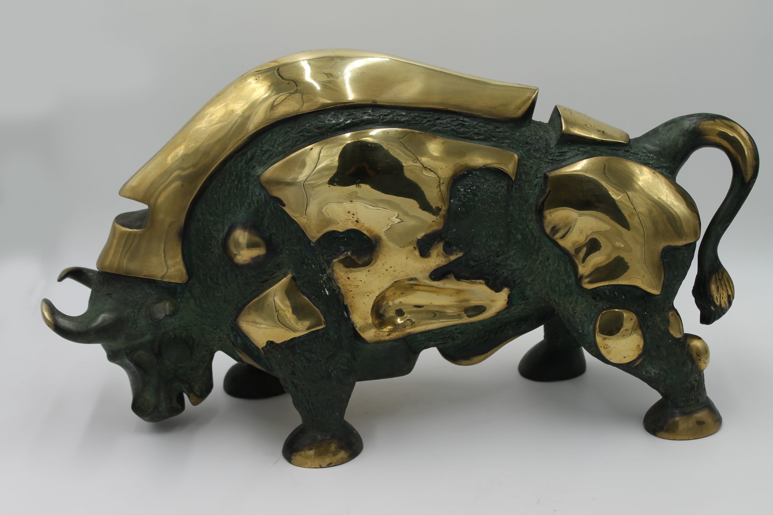 A abstract bronze sculpture of a bull with various patches of gold colouring over it.