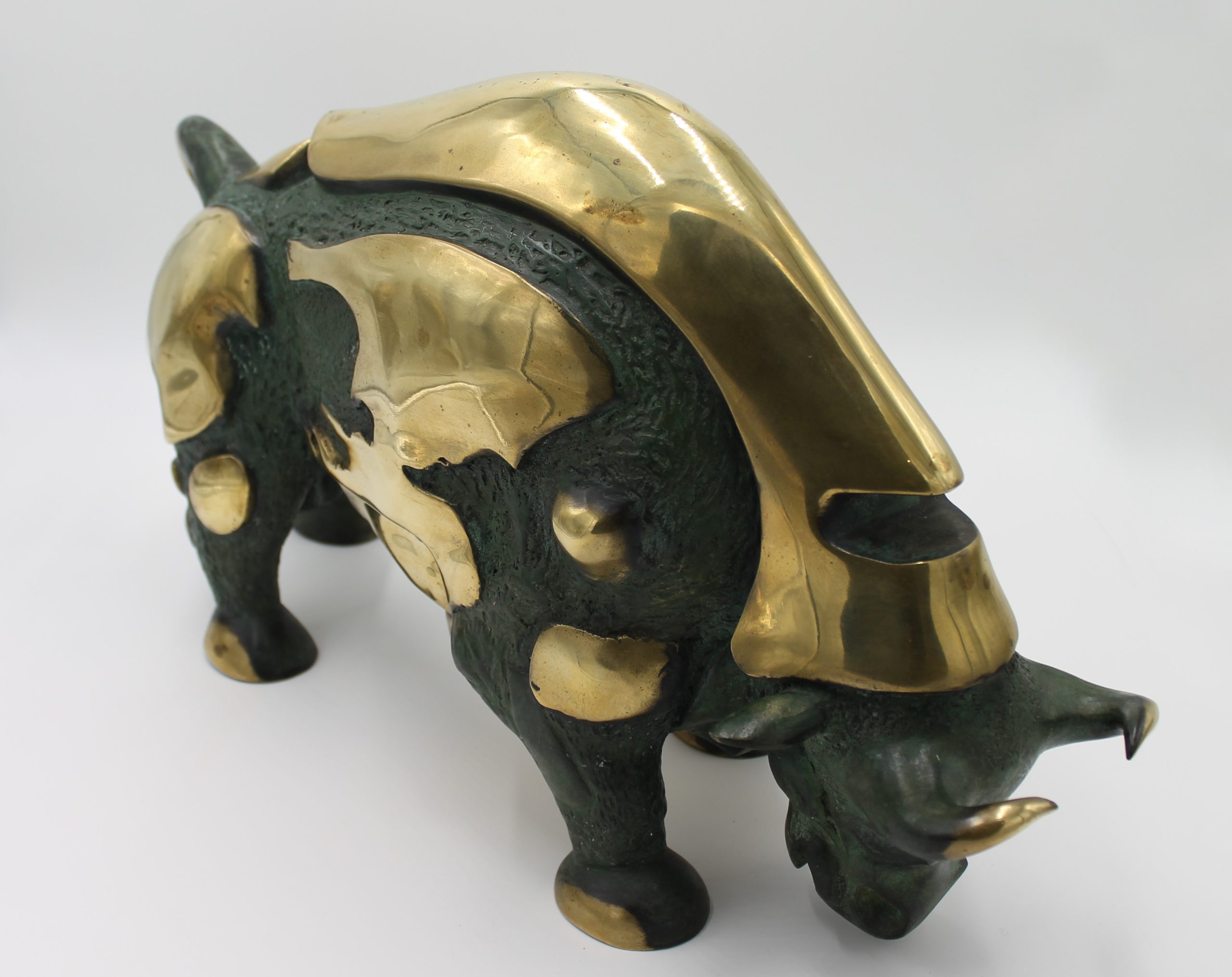 A abstract bronze sculpture of a bull with various patches of gold colouring over it.