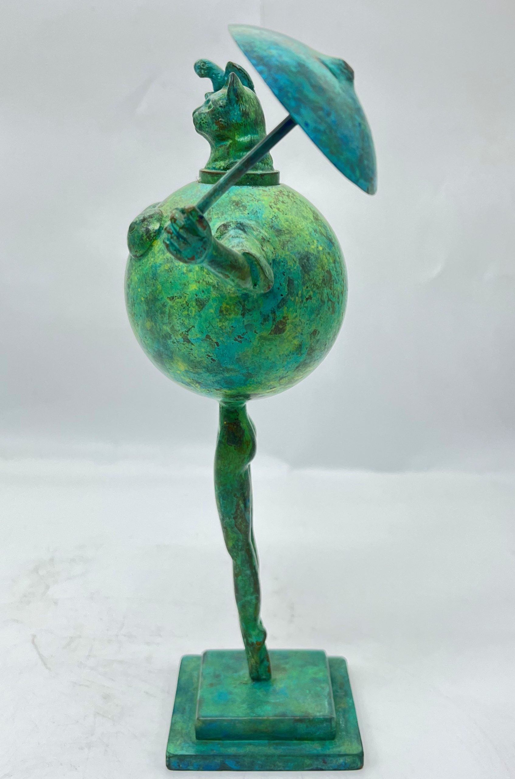 A modern and abstract smaller scale sculpture of a cat stood up straight whilst holding a bird in one hand and an umbrella in the other.