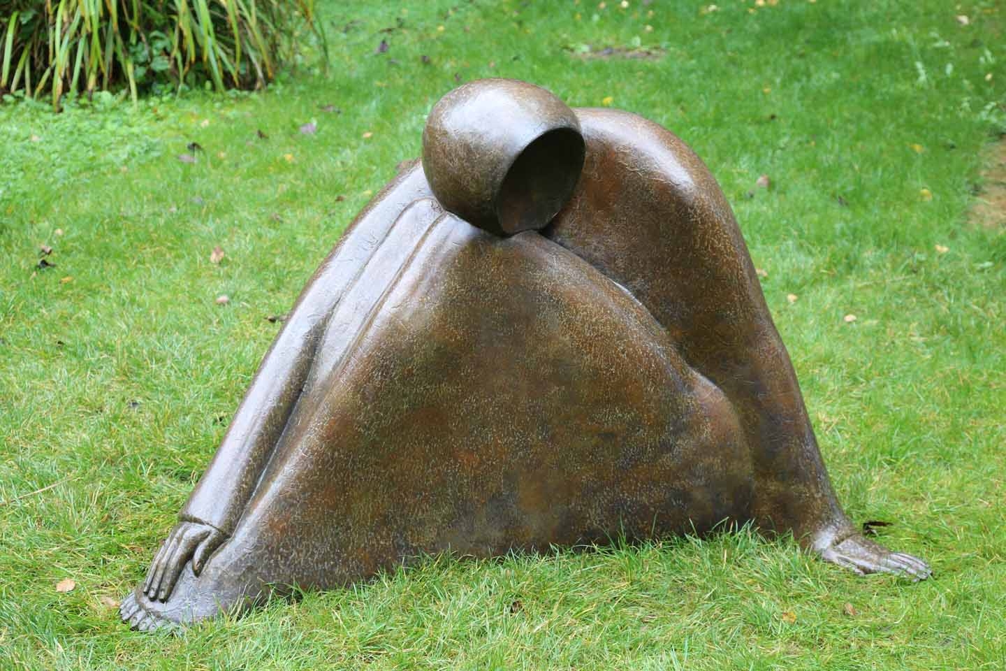 A figurative bronze sculpture of a faceless person sitting down.