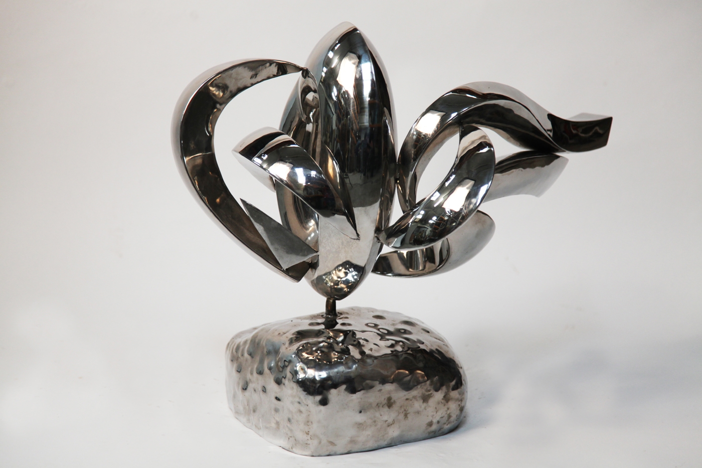 A abstract stainless steel sculpture of different curves and shapes, mounted onto a block.