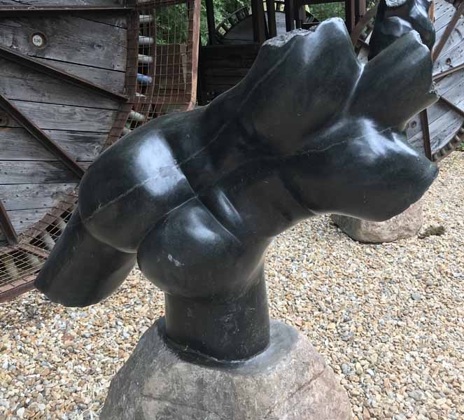 A figurative stone sculpture of a male torso in a expressive pose.