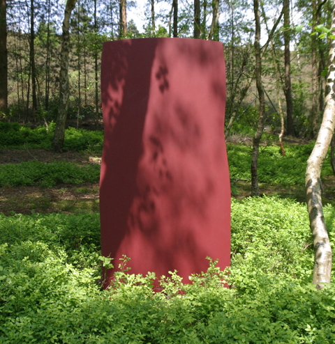 A abstract painted steel sculpture of a large red block of metal.