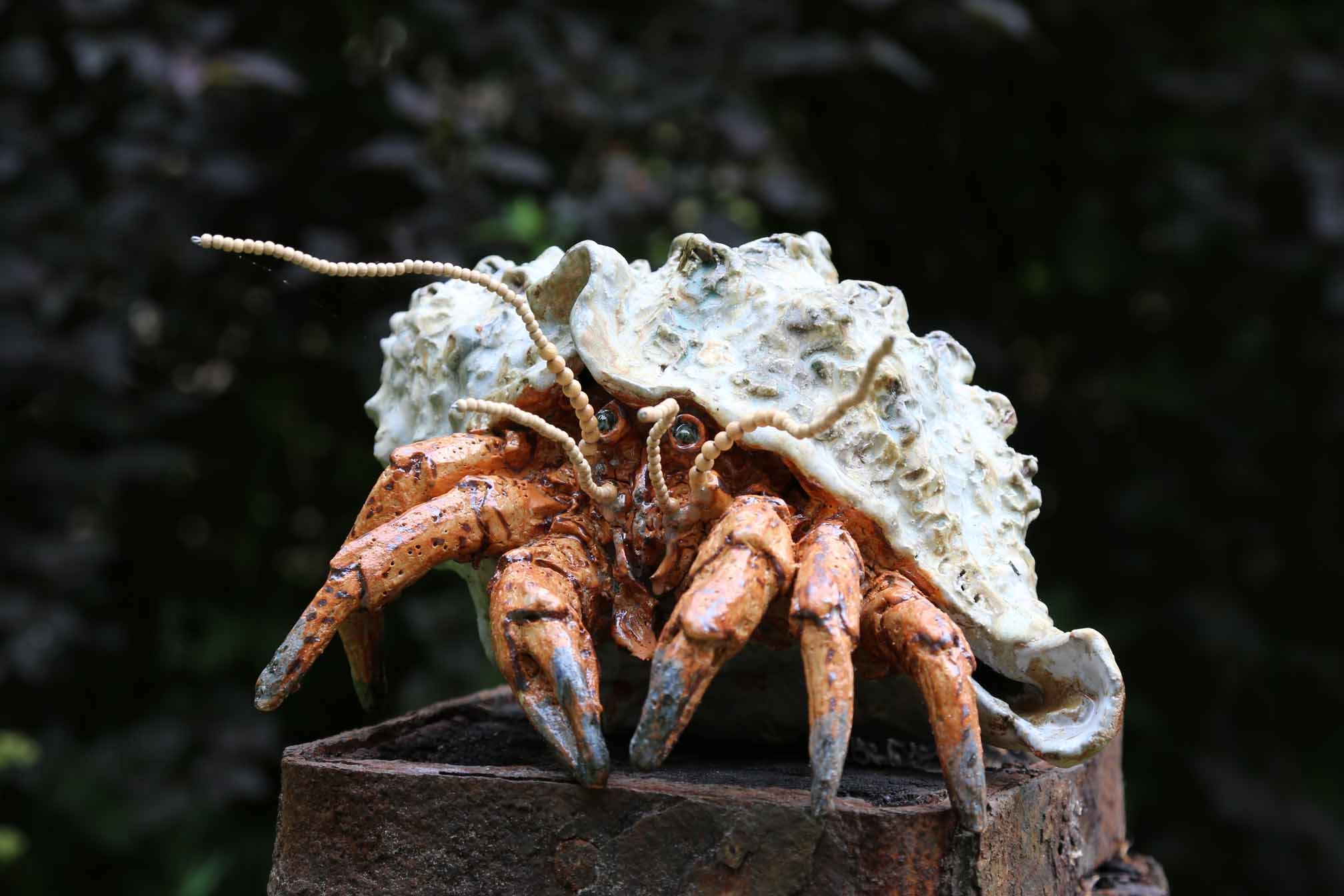 A figurative stoneware sculpture of a hermit crab crawling out of its shell.