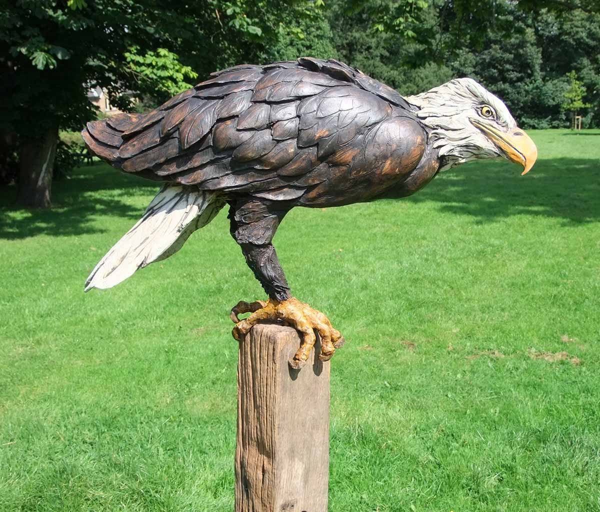 A natural stoneware sculpture of a bald eagle perched on top of a block of wood.