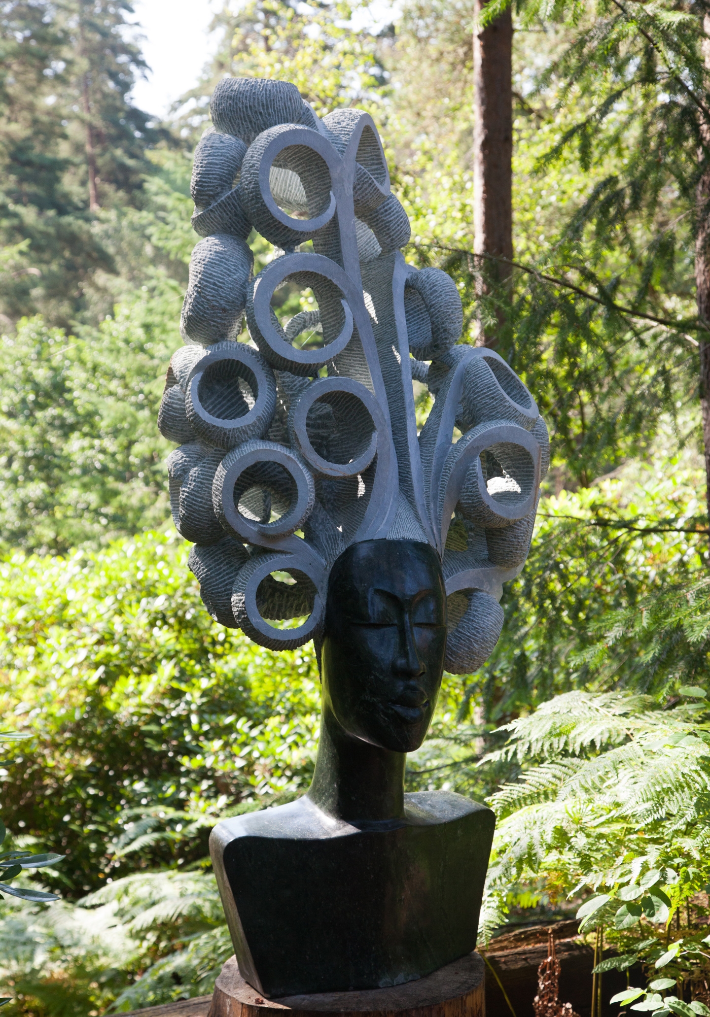 A large scale Shona sculpture depicting a woman's head and shoulders, with large curly hair.