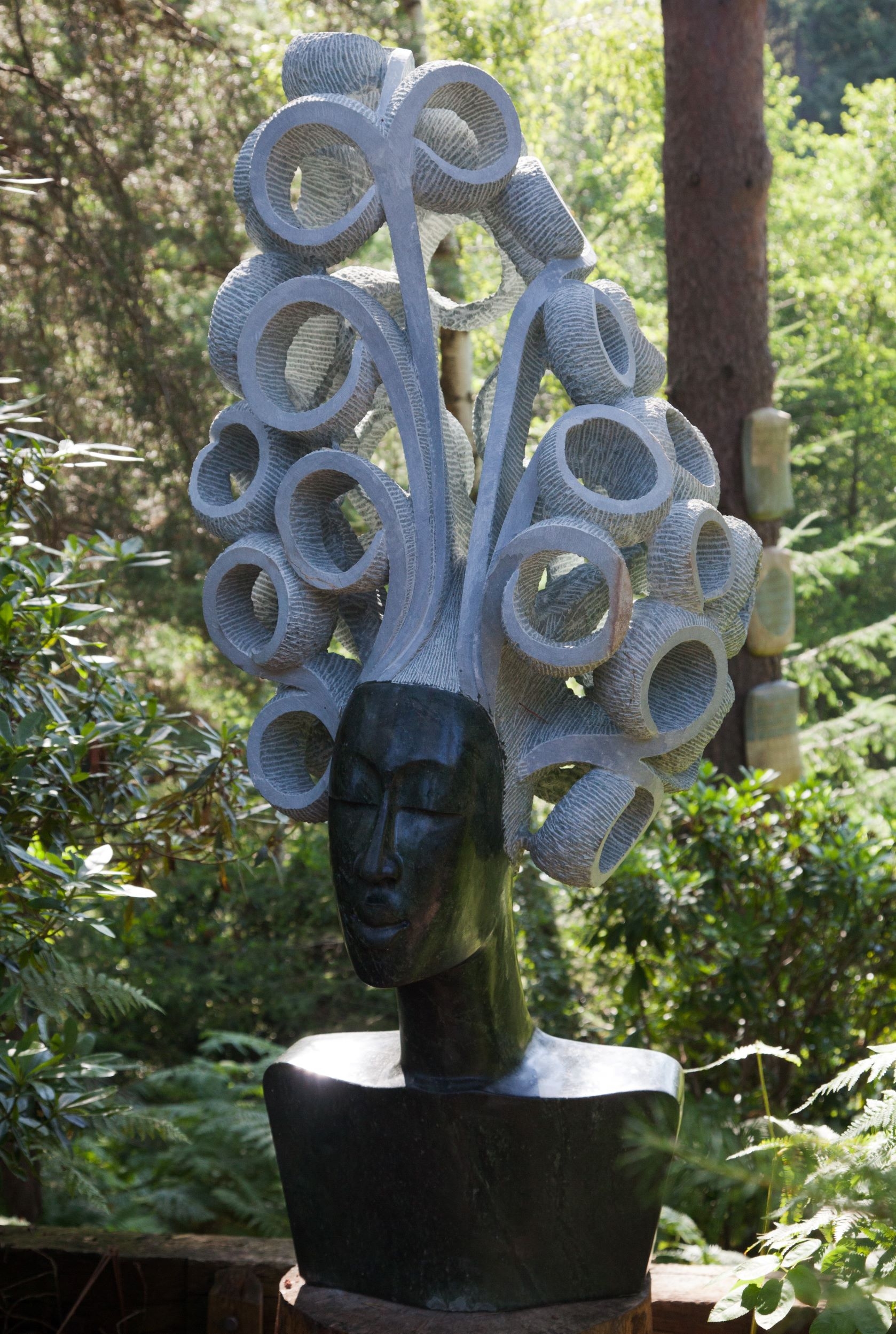 A large scale Shona sculpture depicting a woman's head and shoulders, with large curly hair.