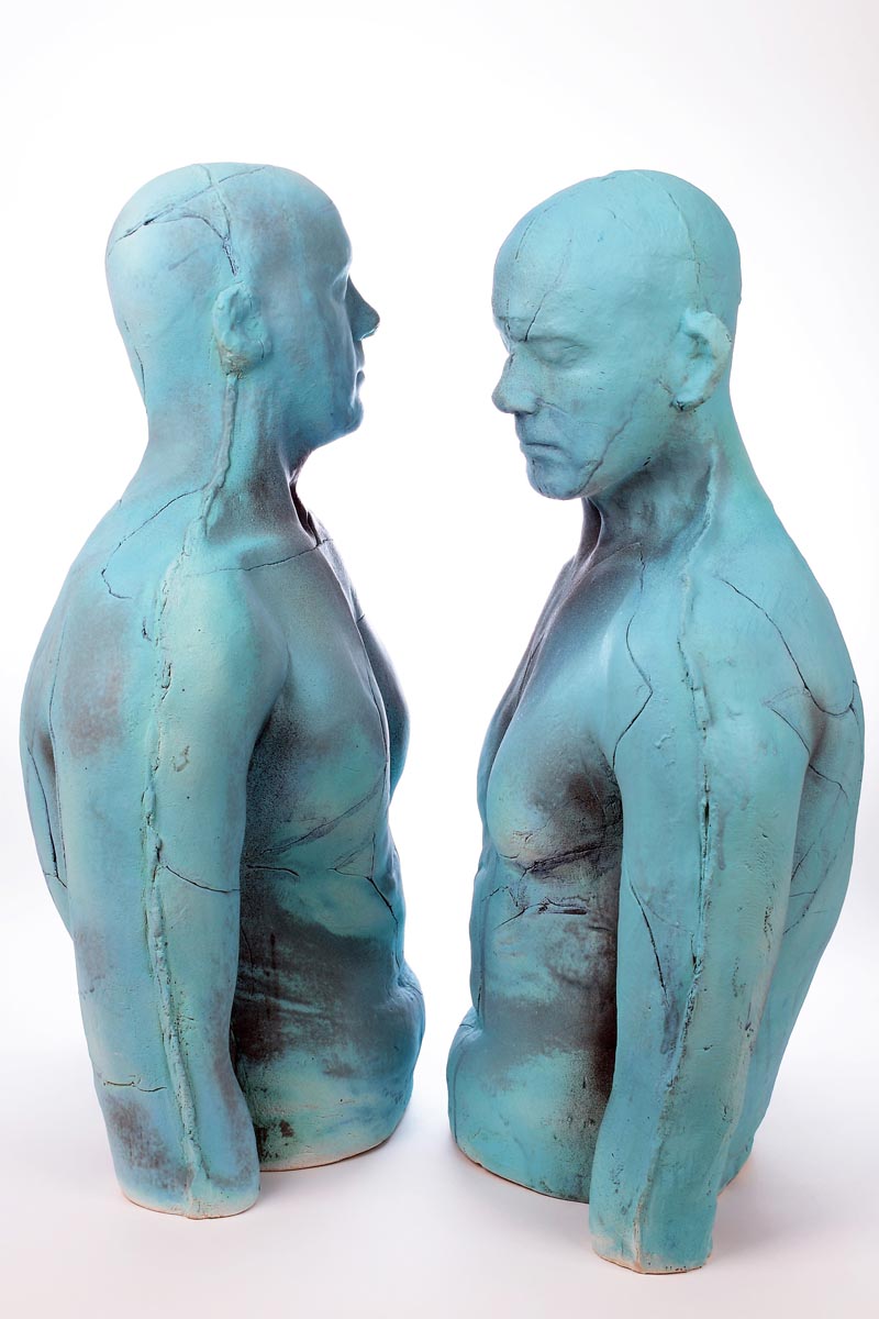 A figurative stoneware ceramic sculpture of two men in front each other yet looking away.