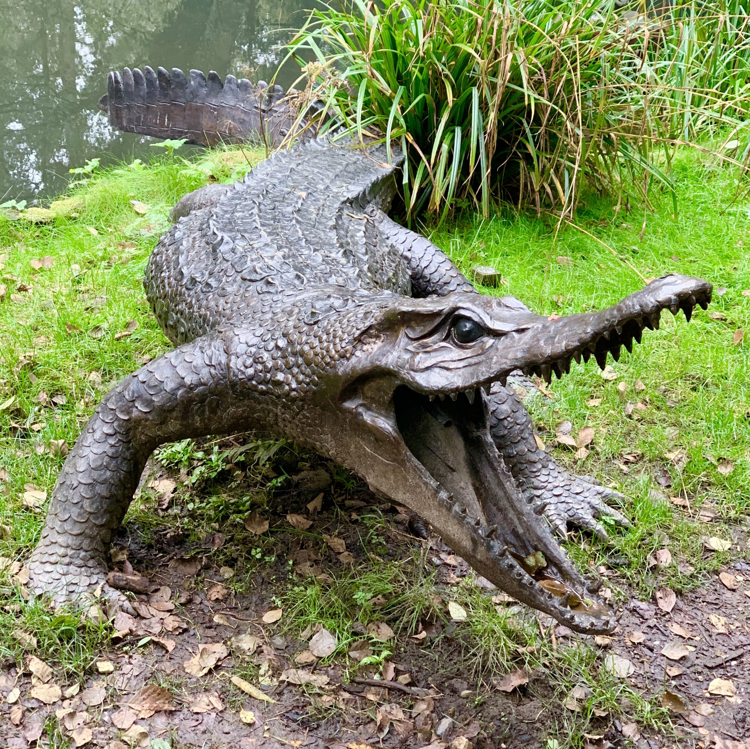 A figurative bronze sculpture of a crocodile walking forwards with its mouth open wide.