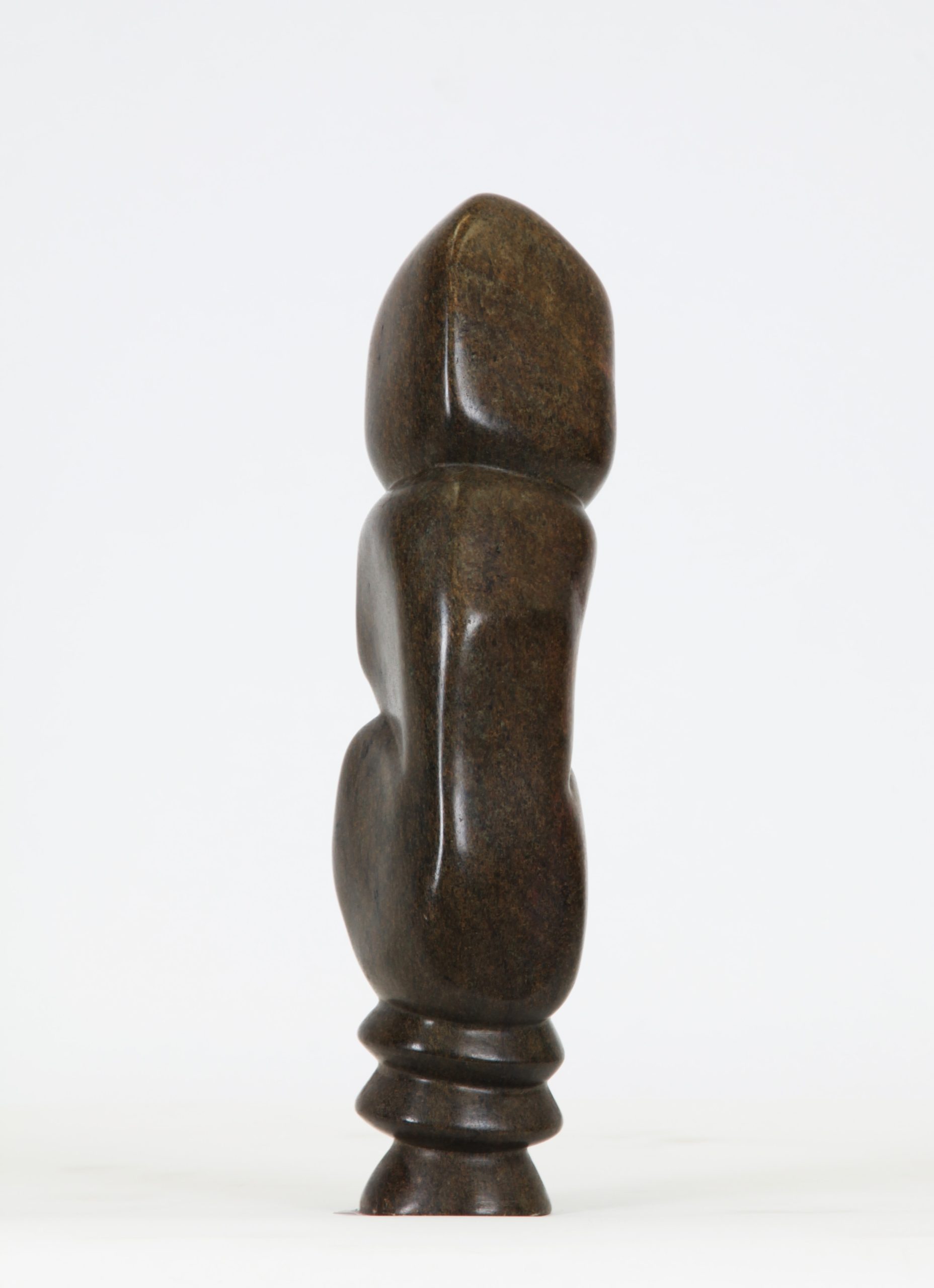 A Shona Serpentine stone sculpture of a person hunched over and hugging themselves.