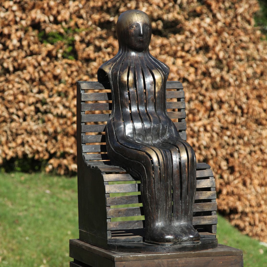 Figure on a Park Bench by Geraldine Knight. Bronze Sculpture of a Woman on a Bench, no arms, striped body
