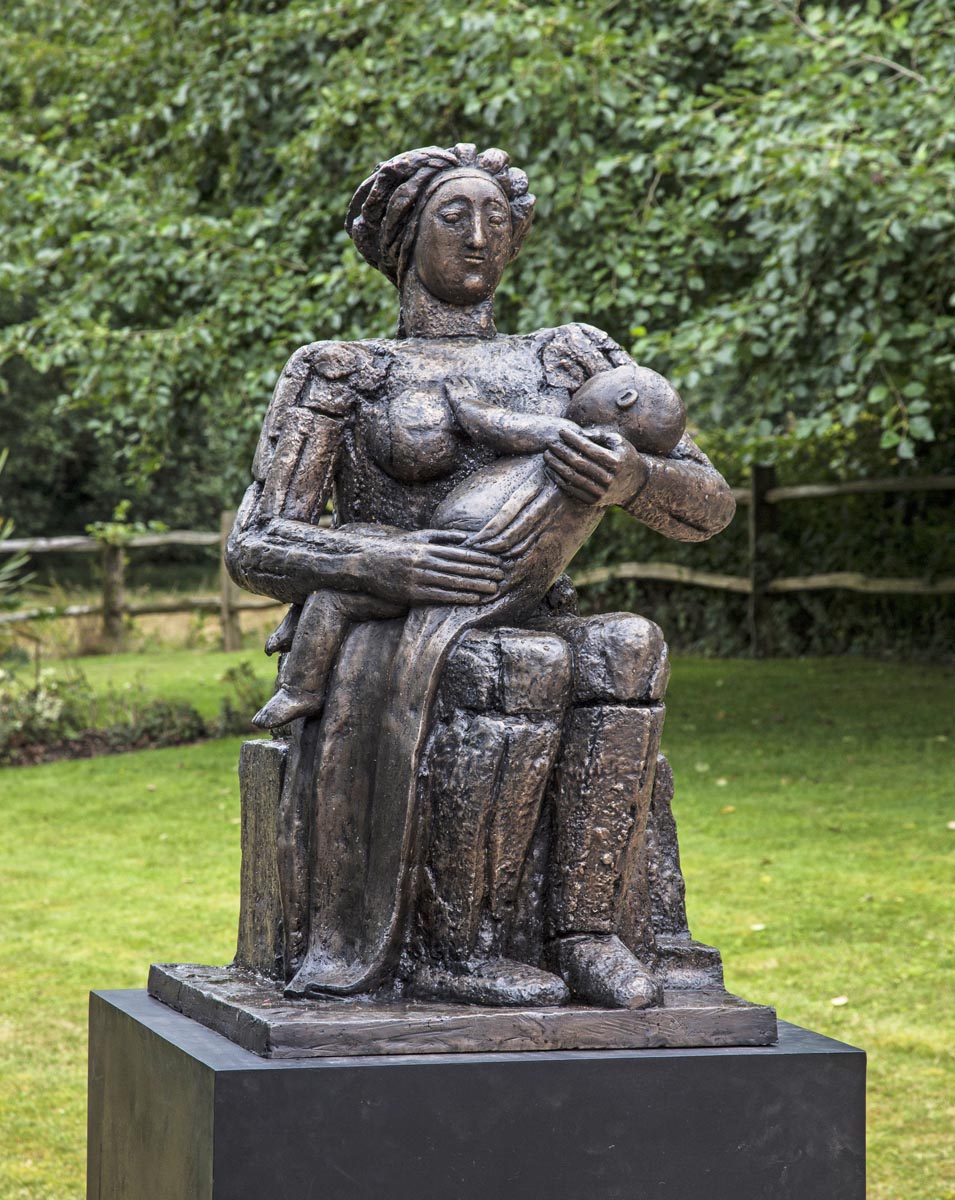 A figurative bronze sculpture of a mother sat down and nursing her baby.