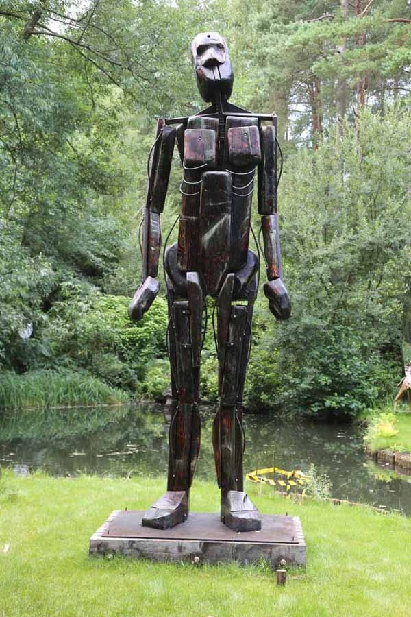 A figurative wood and steel sculpture of a man standing.