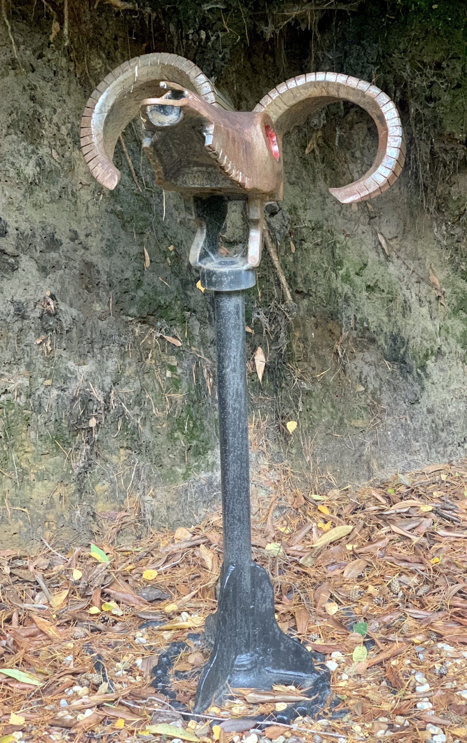 A abstract salvaged steel sculpture of a goats head mounted onto a stand.