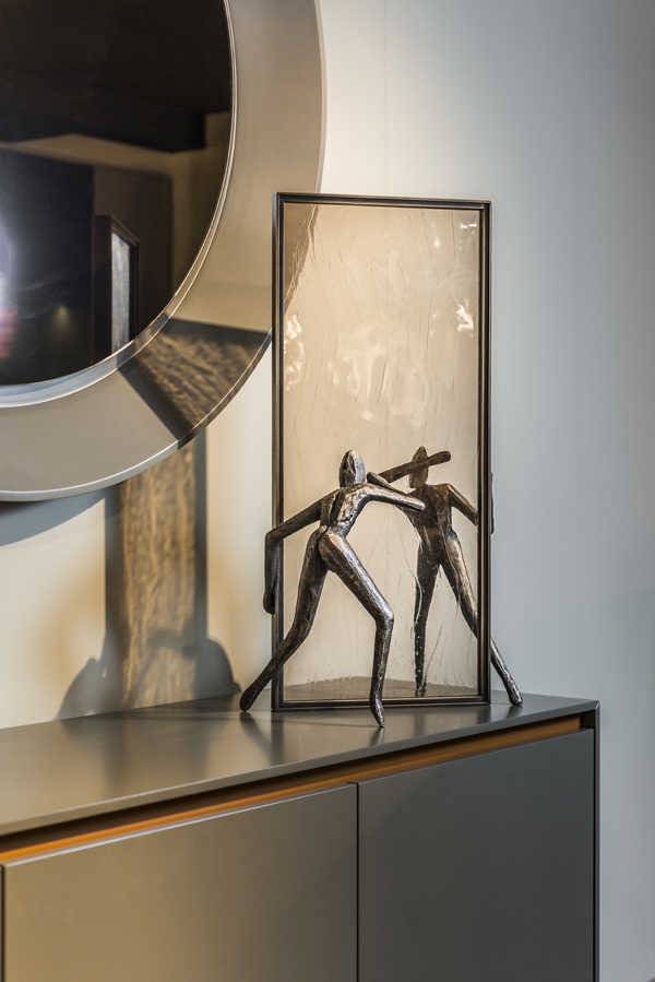 A figurative bronze sculpture of two figures looking though a mirror to see each other.