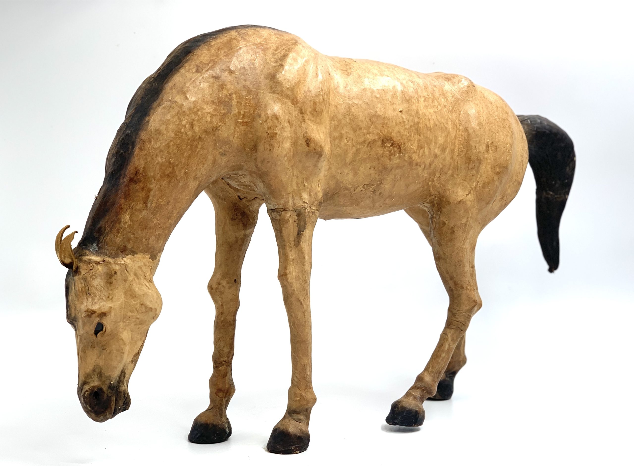 A realism figurative leather sculpture of a dun coloured horse with its head down.