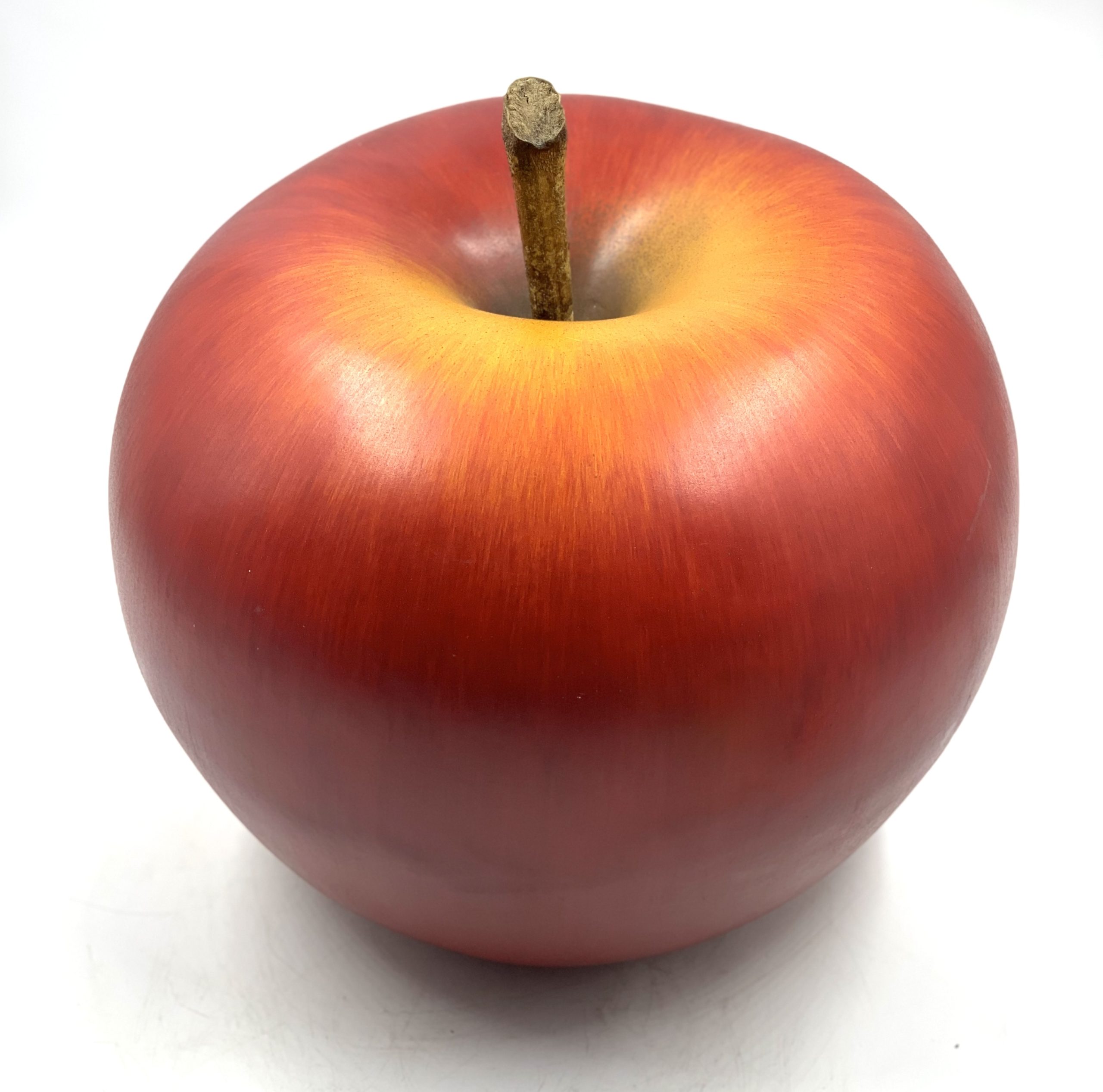 A realism ceramic sculpture of a shiny red and yellow apple with part of the stalk still attached.