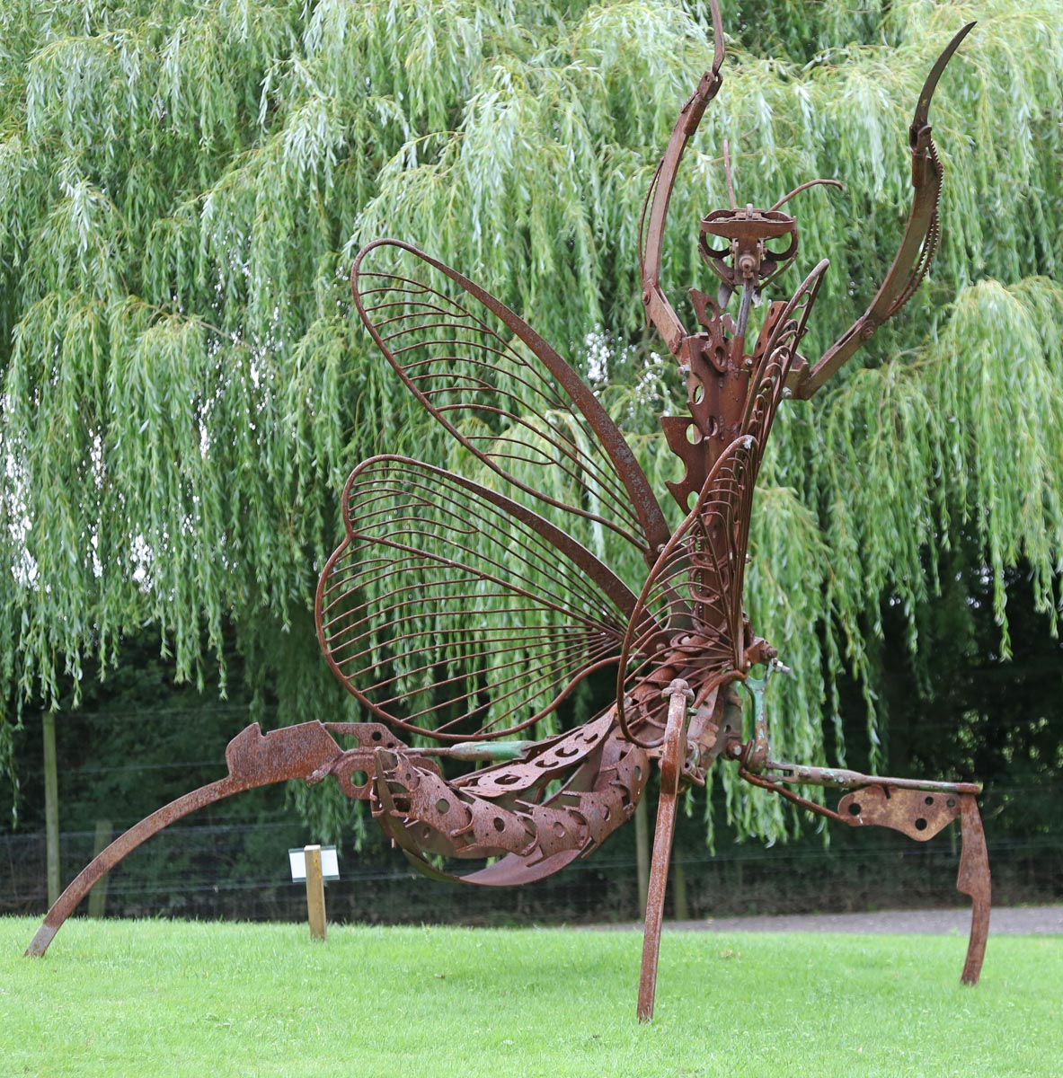 A figurative steel sculpture of a preying mantis with its arms raised up.
