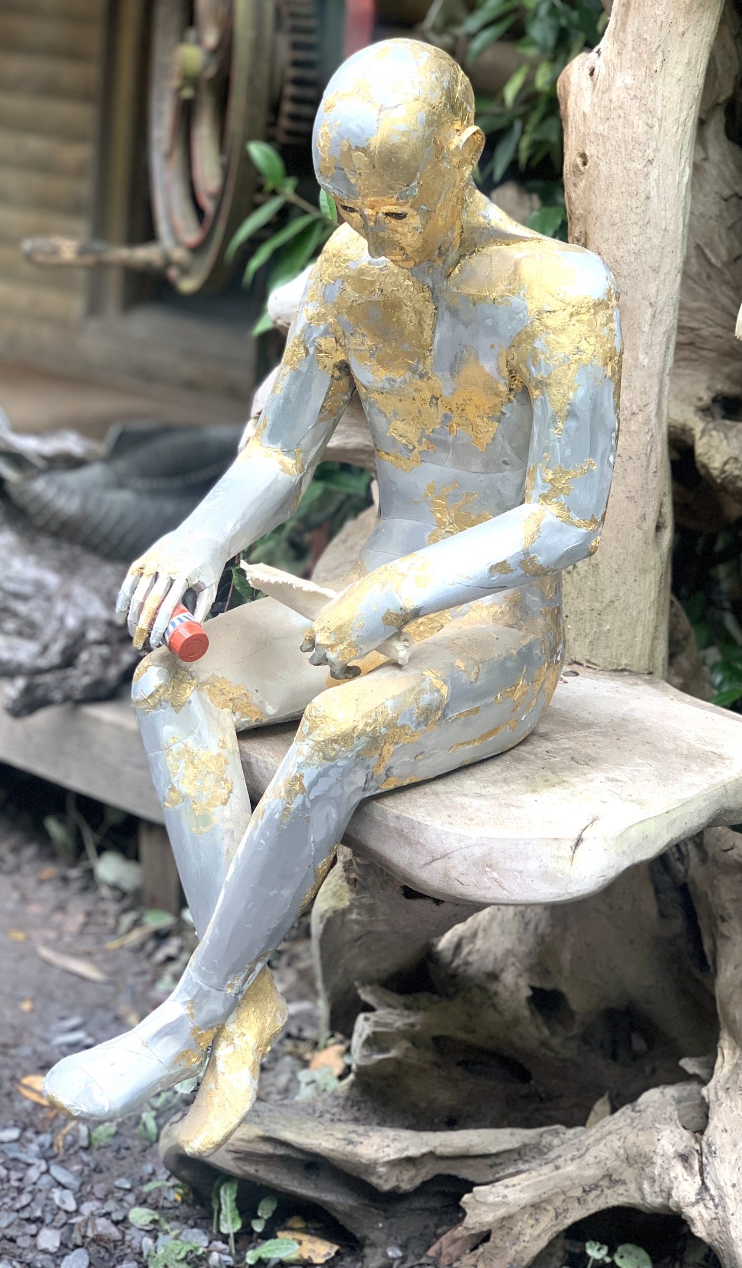 A abstract figurative sculpture of a man sitting while holding two items, made from aluminium.