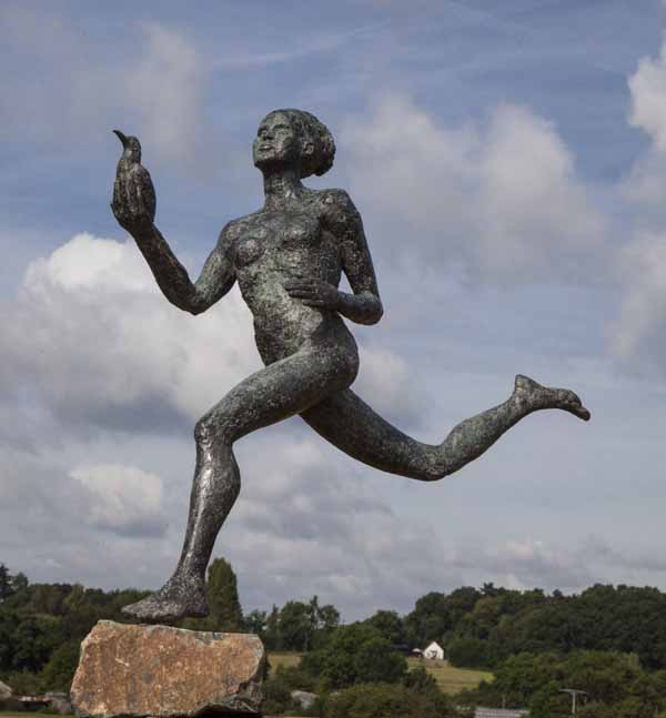 A figurative bronze sculpture of a person running while holding a bird in one hand.