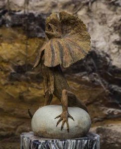 A figurative stoneware sculpture of a frilled lizard standing on top of a rock.