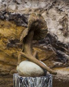 A figurative stoneware sculpture of a frilled lizard standing on top of a rock.